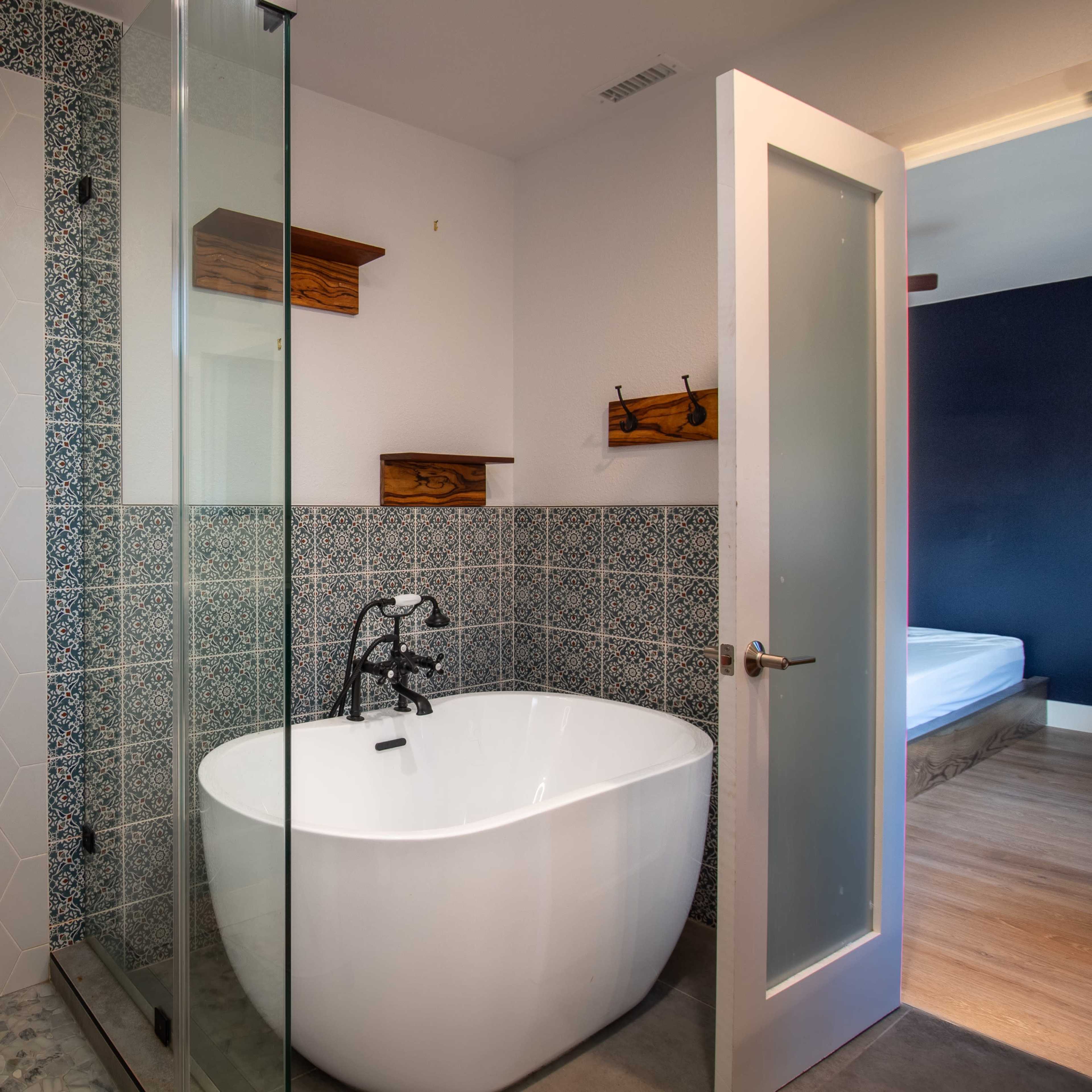A modern bathroom featuring a glass-enclosed shower with a hexagonal tile design, a freestanding bathtub, and wooden shelves.