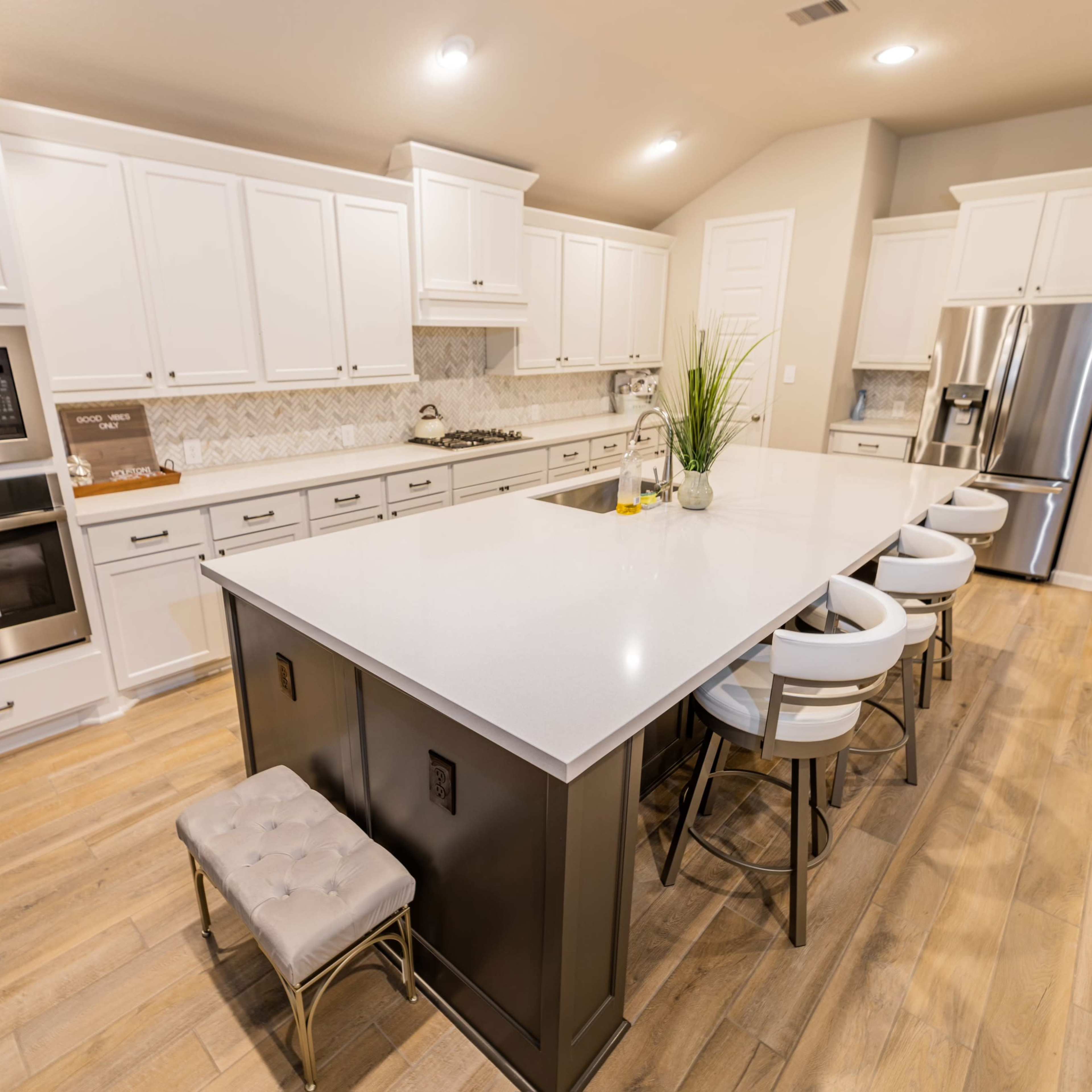 The kitchen features white cabinetry, a large central island with bar stools, and stainless steel appliances.