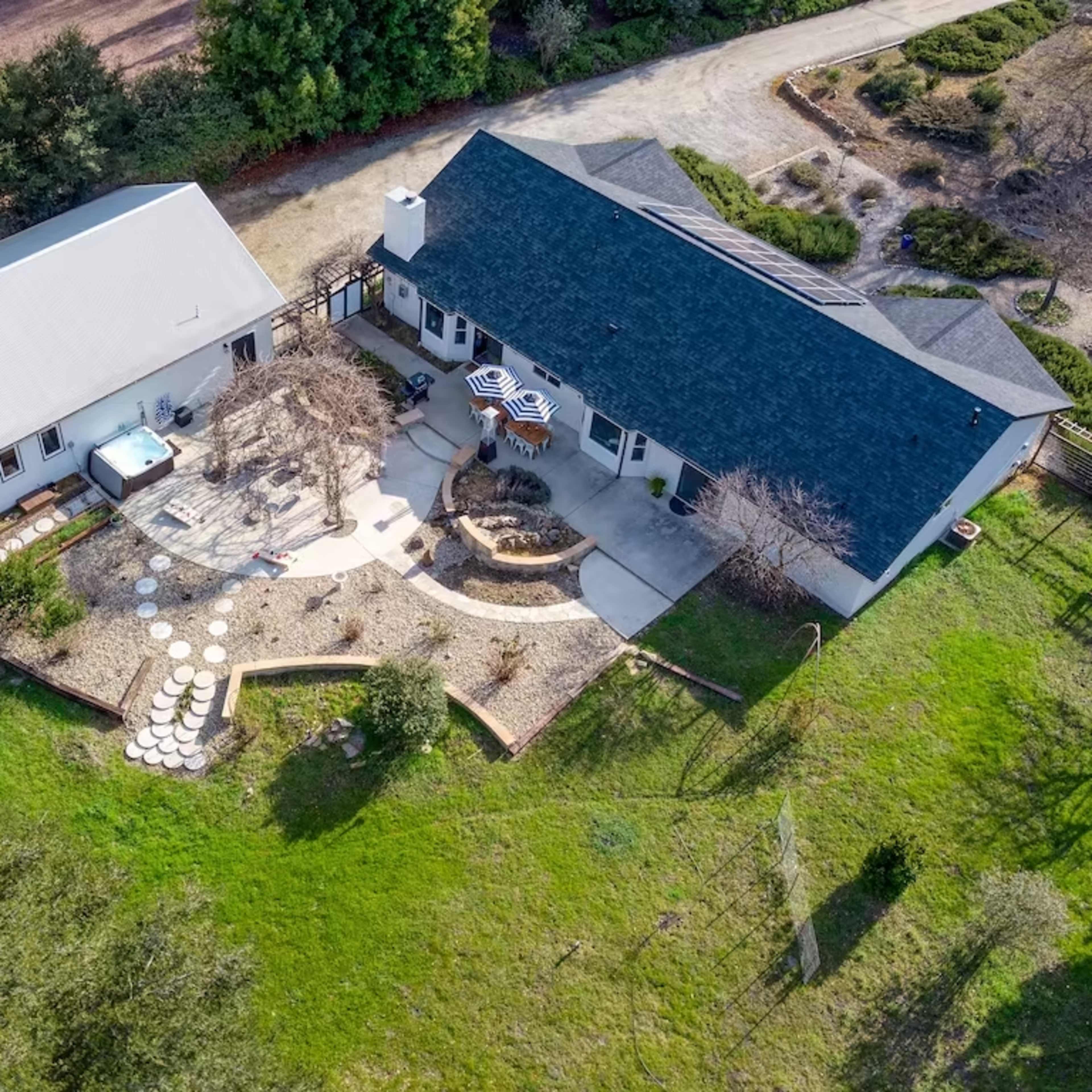 A large property featuring two buildings, a patio area with outdoor seating, and landscaped gardens.
