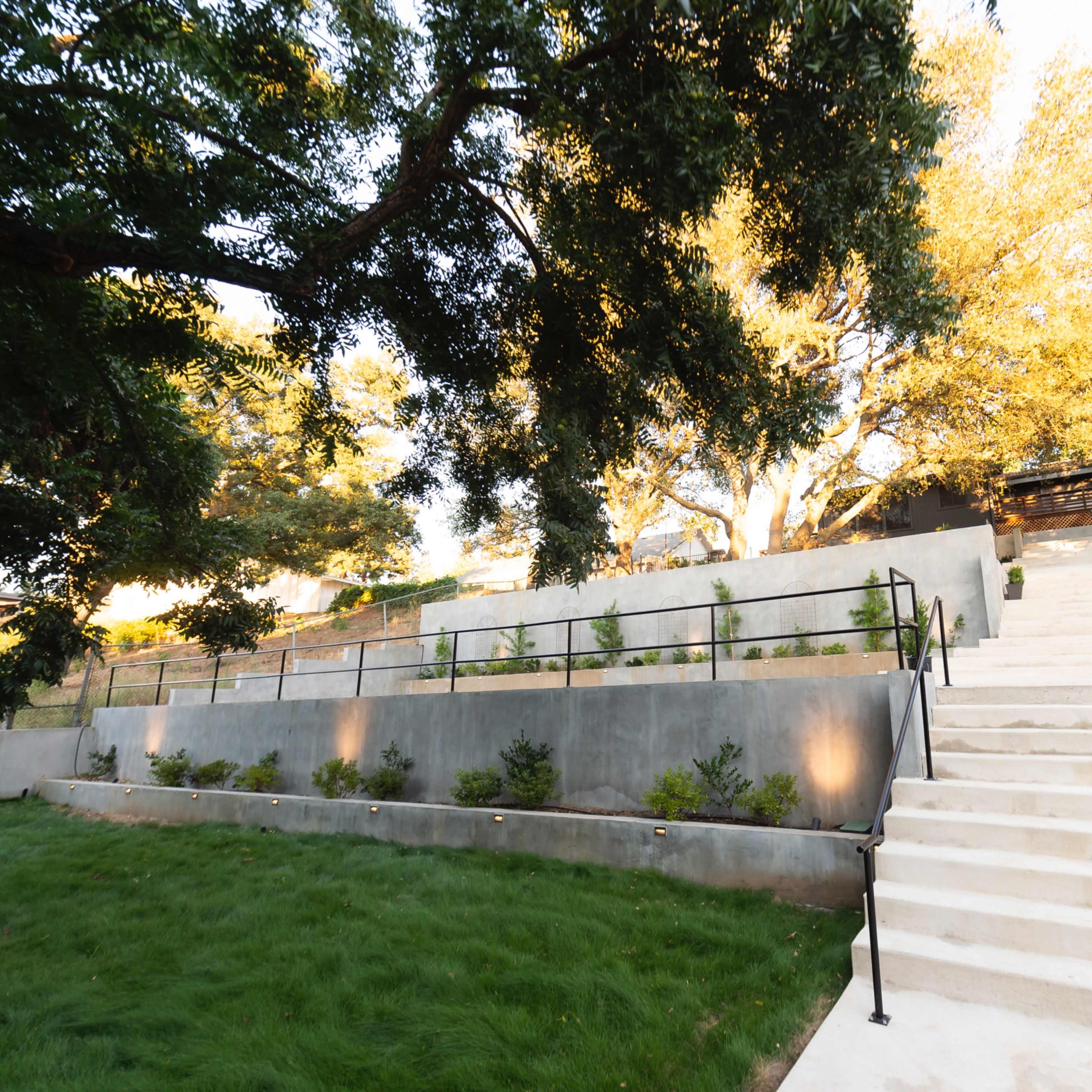 A set of wide concrete stairs leads upward through a landscaped area with trees and planted beds.