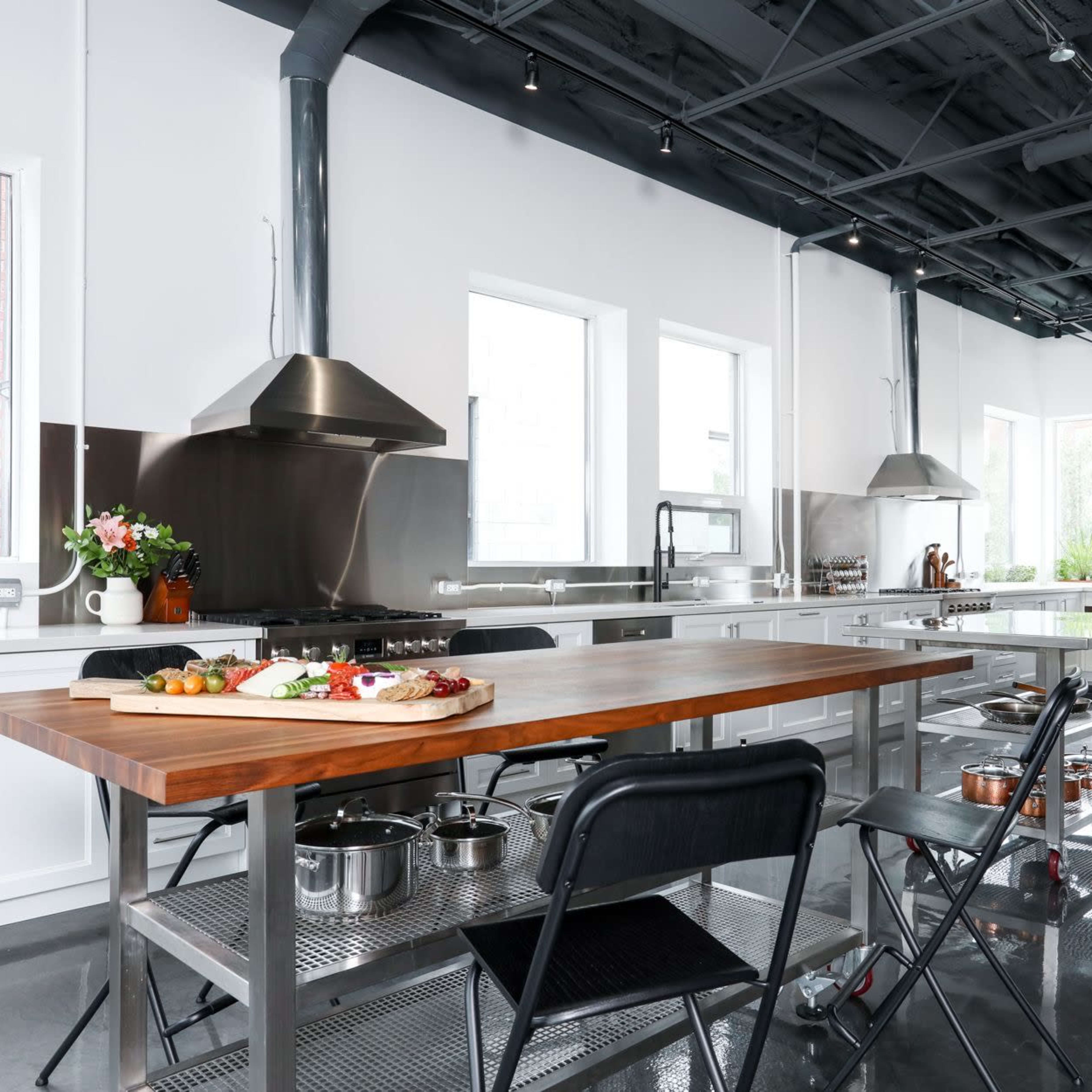 A modern kitchen featuring a large wooden island, stainless steel appliances, and bright windows with a view of greenery outside.