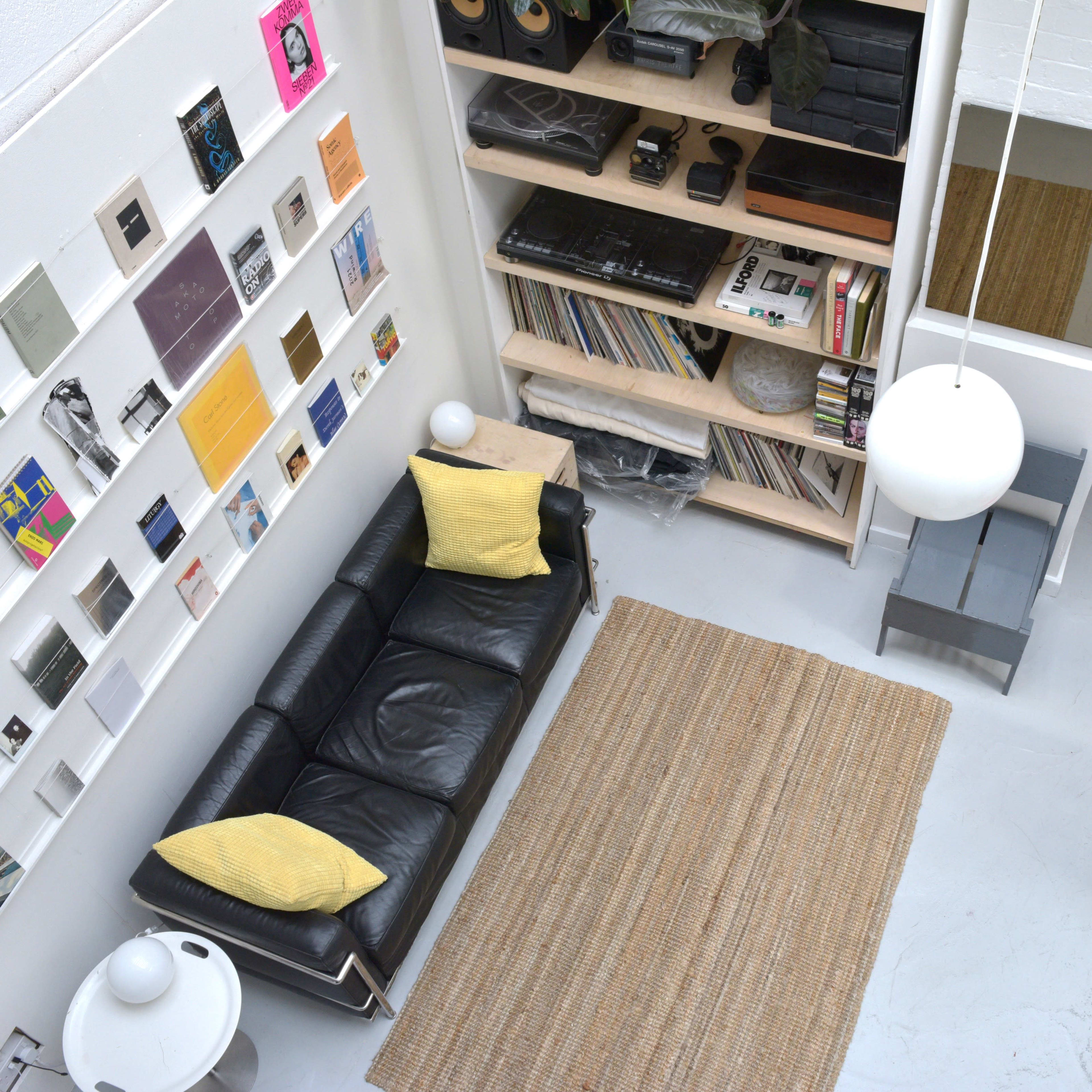 A modern living space featuring a black leather sofa, a light-colored rug, and a wall adorned with various framed artworks and vinyl records.