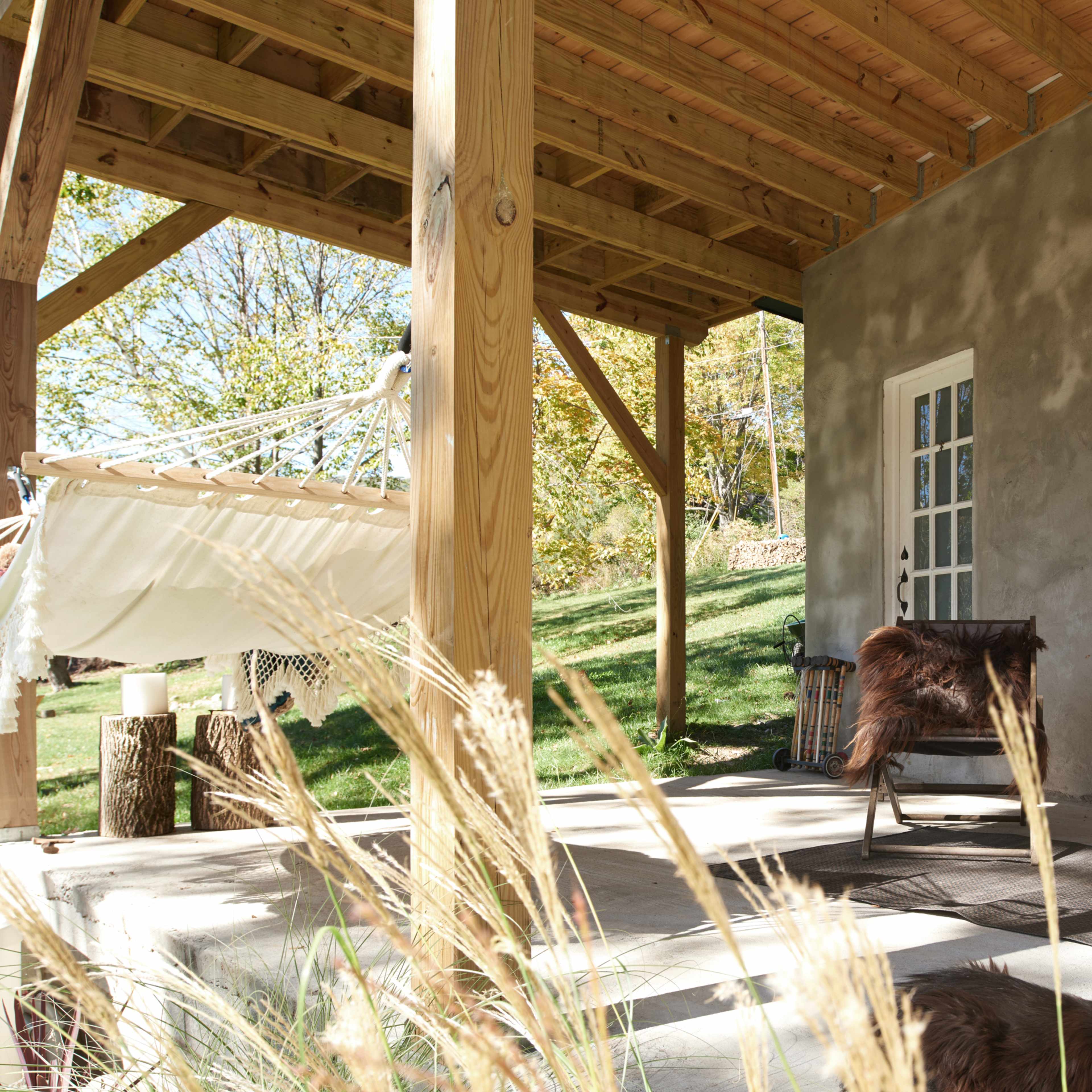A shaded patio features wooden posts, two lounging chairs, and a hammock, with a grassy area visible in the background.