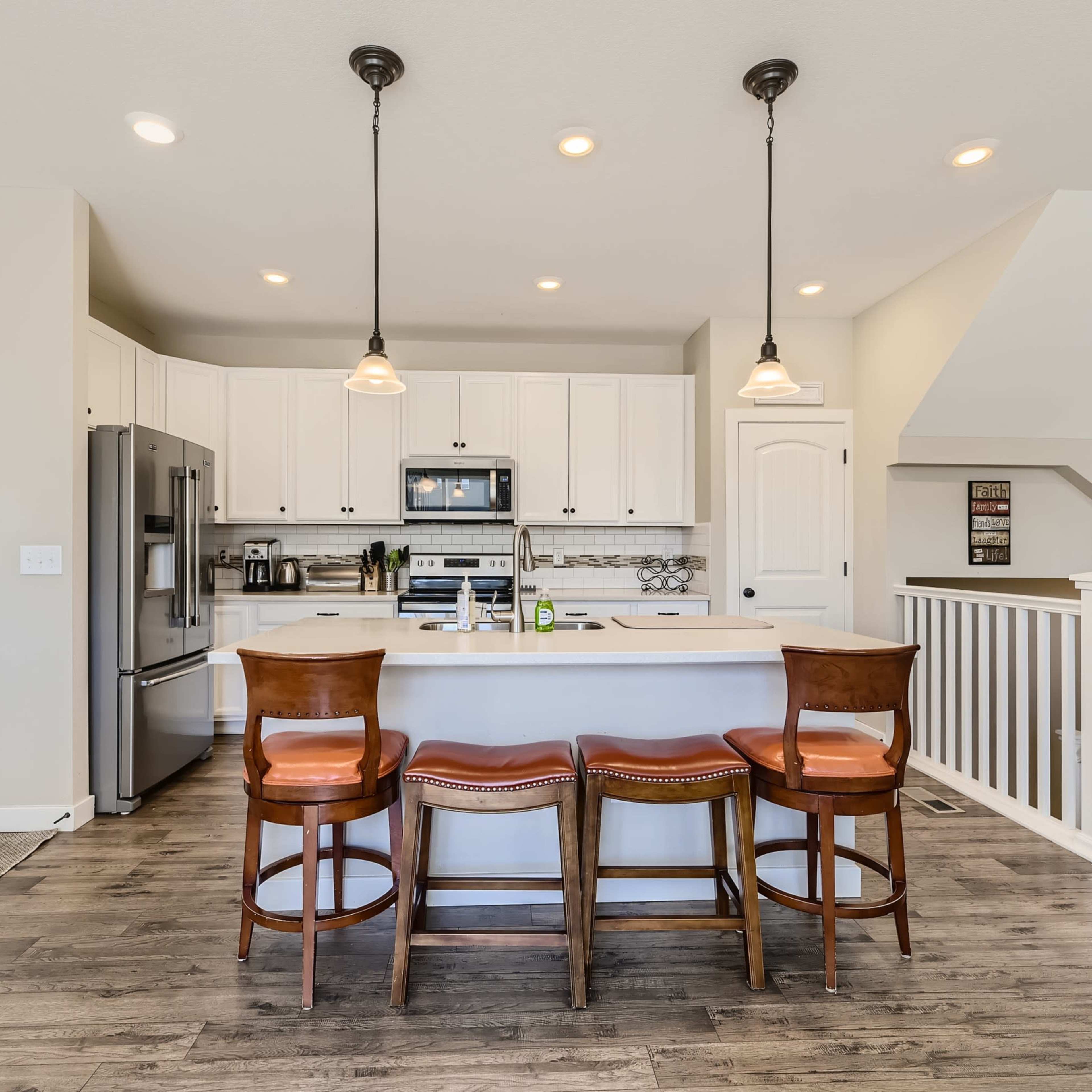 A bright kitchen features white cabinetry, stainless steel appliances, a central island with seating, and hardwood flooring.