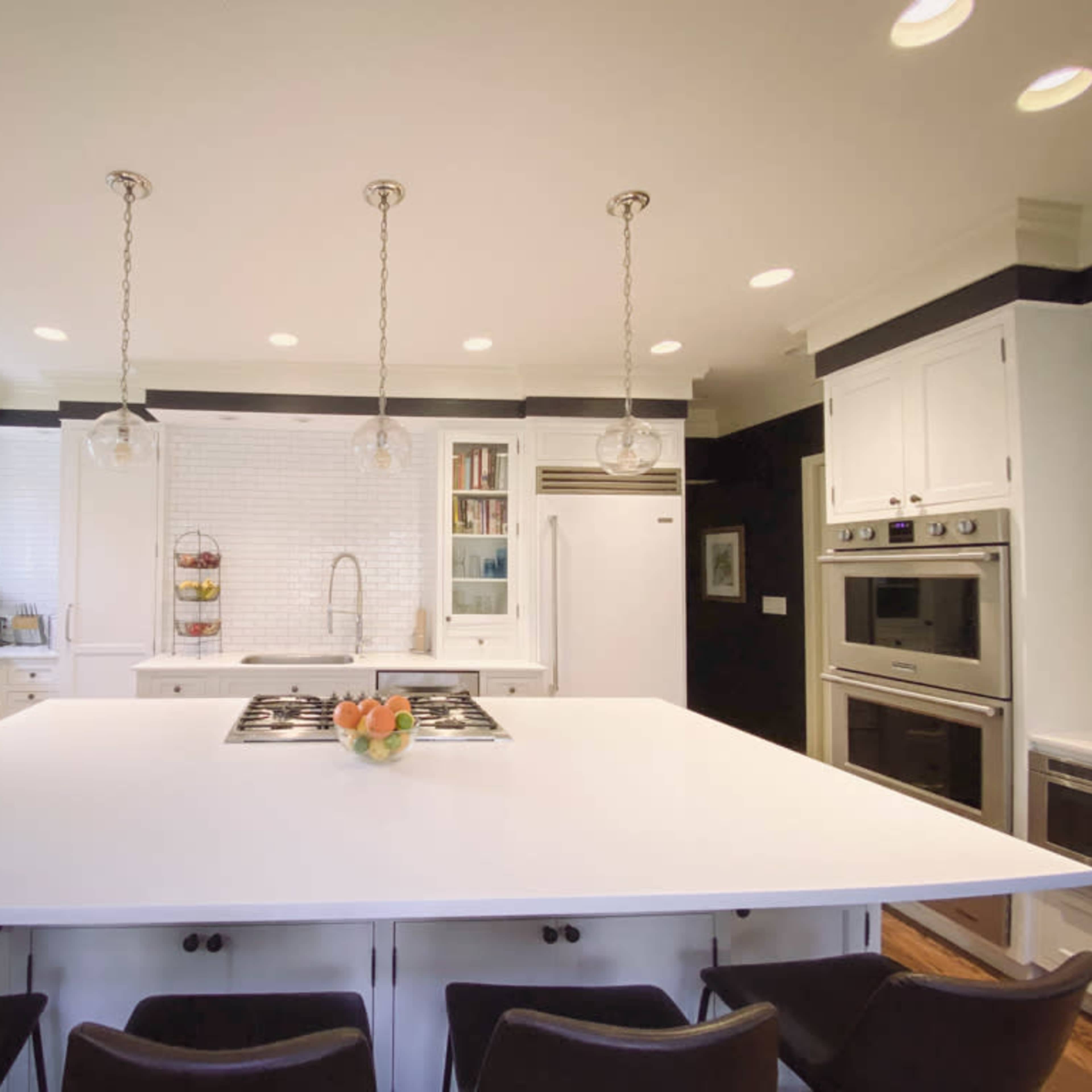 A modern kitchen features a large white island with bar seating, stainless steel appliances, and a backsplash of white tiles.