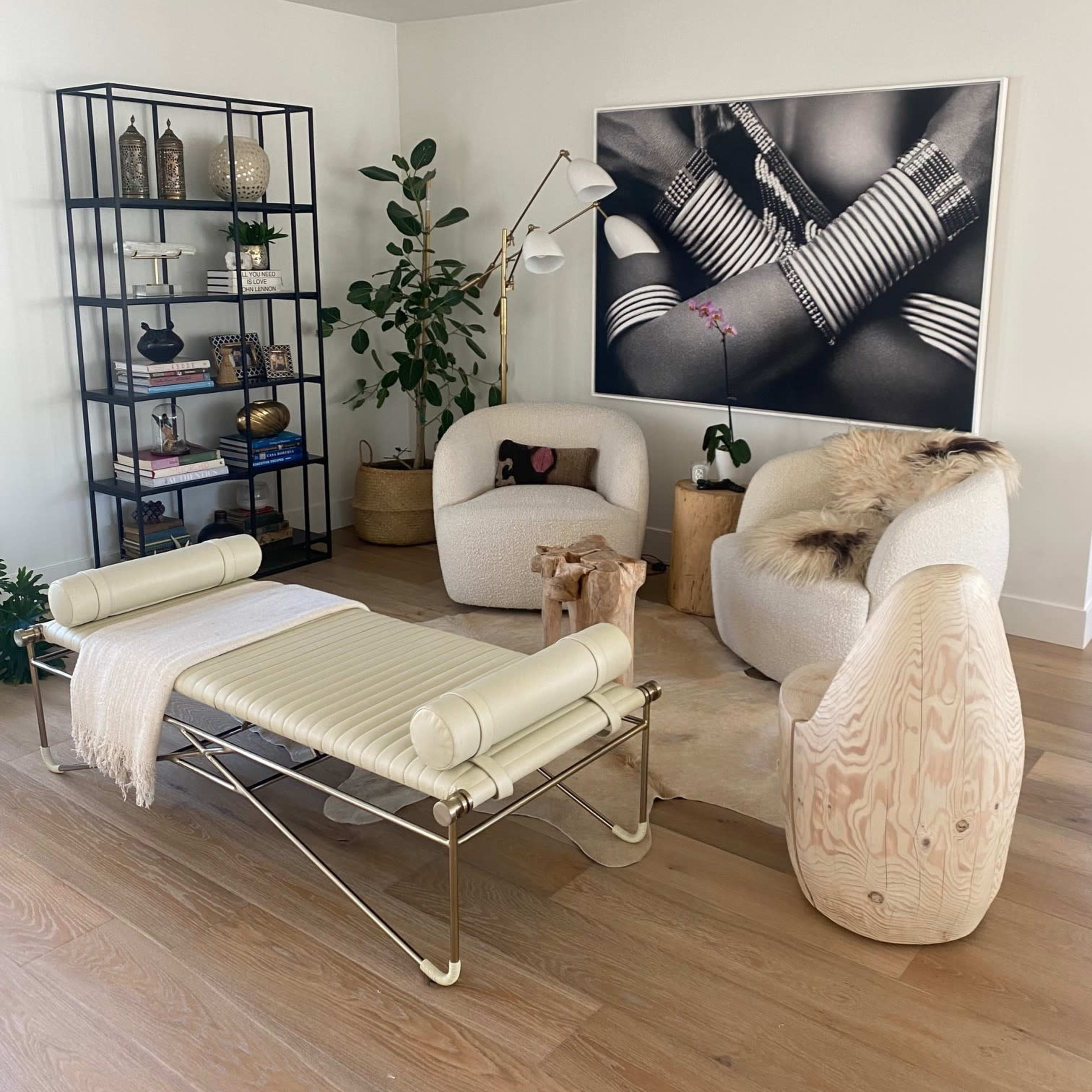 A modern living room with two upholstered chairs, a bench, and a bookshelf, featuring decorative items and a large black and white photograph on the wall.
