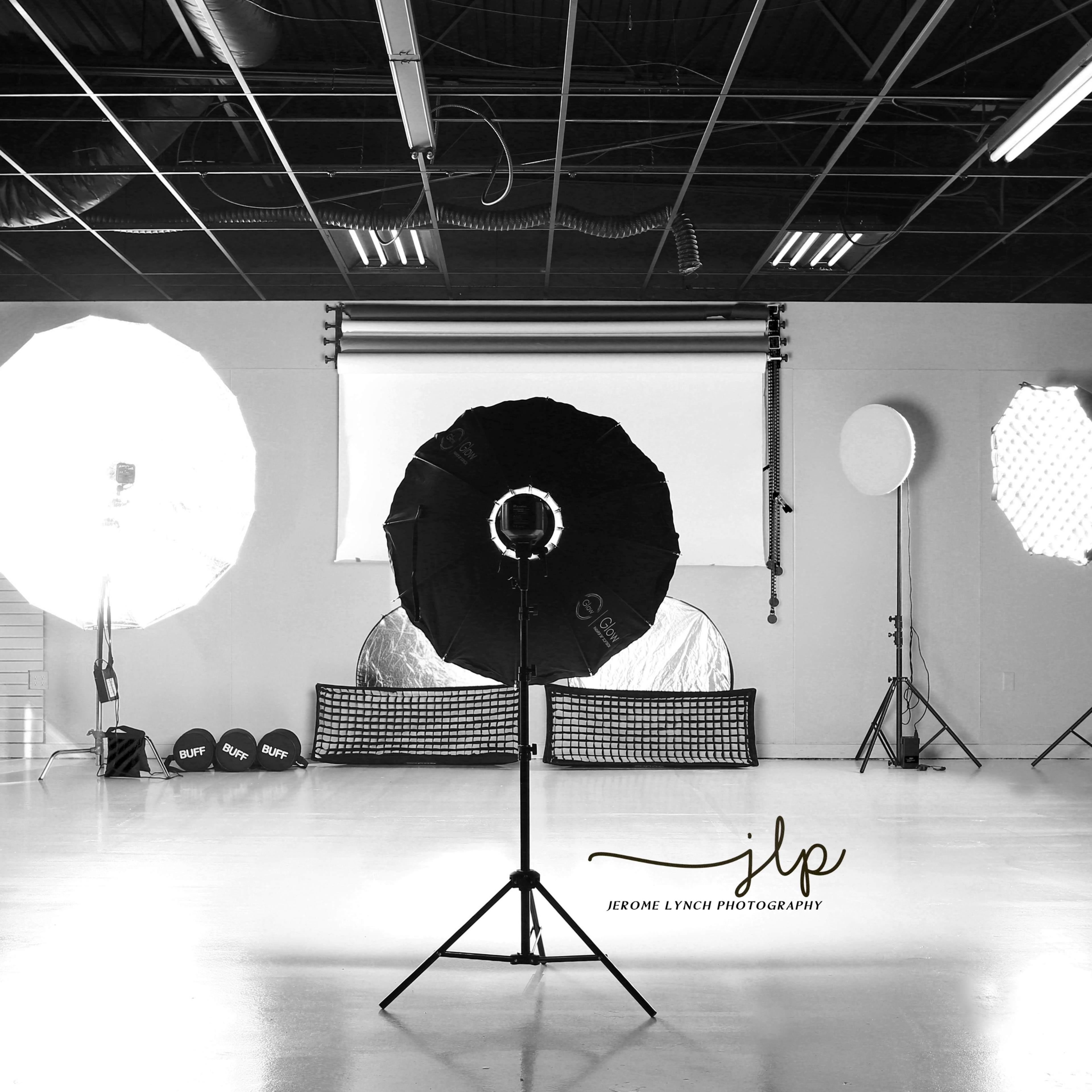 A photography studio with various lighting equipment, including softboxes and a ring light, arranged around a backdrop.