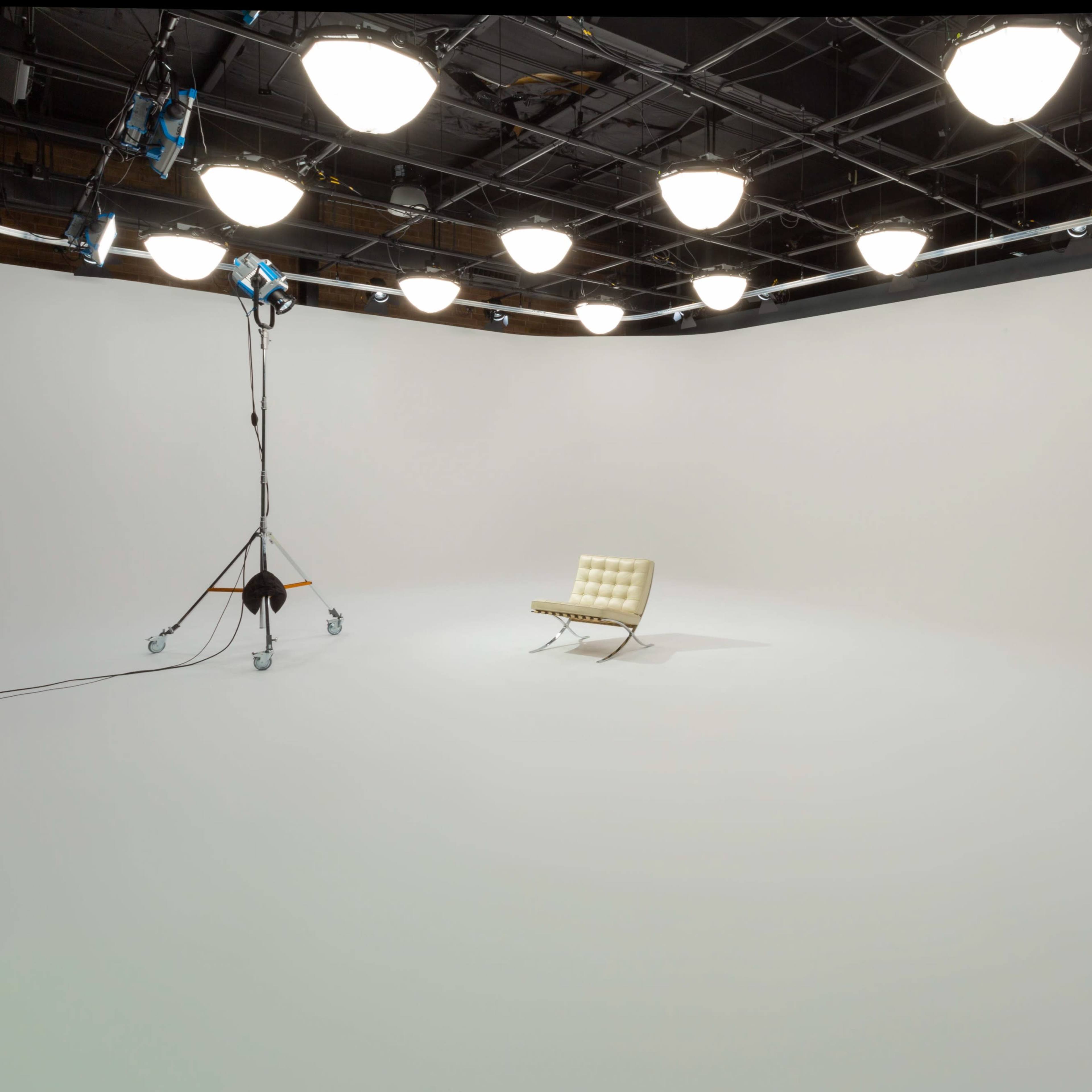 A bright, empty studio room features a single light-colored chair on a white backdrop, illuminated by overhead lights.