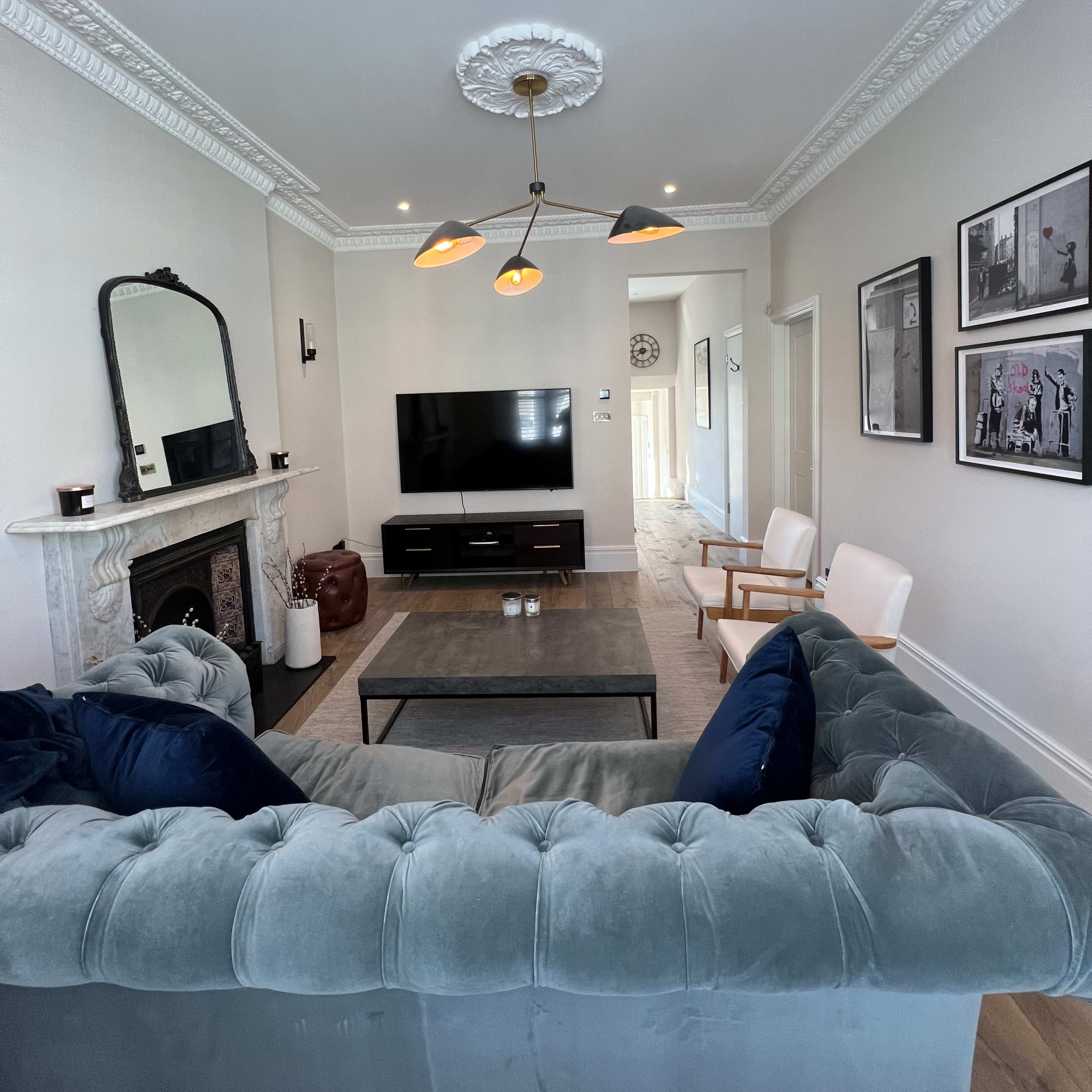 A modern living room featuring a velvet sofa, a coffee table, a television mounted on the wall, and decorative artwork.