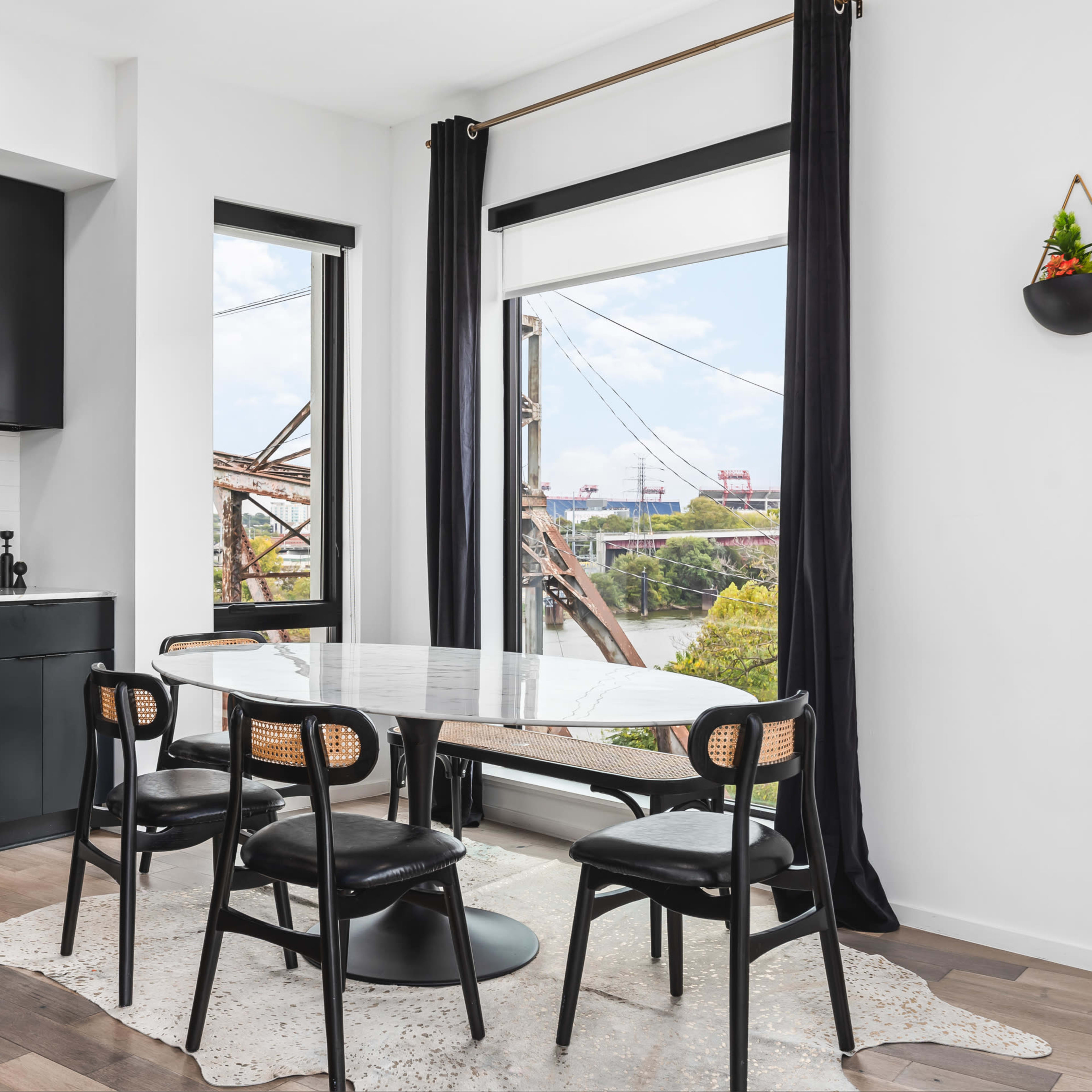 A modern kitchen with black cabinets, a marble dining table, and views of a bridge through large windows.