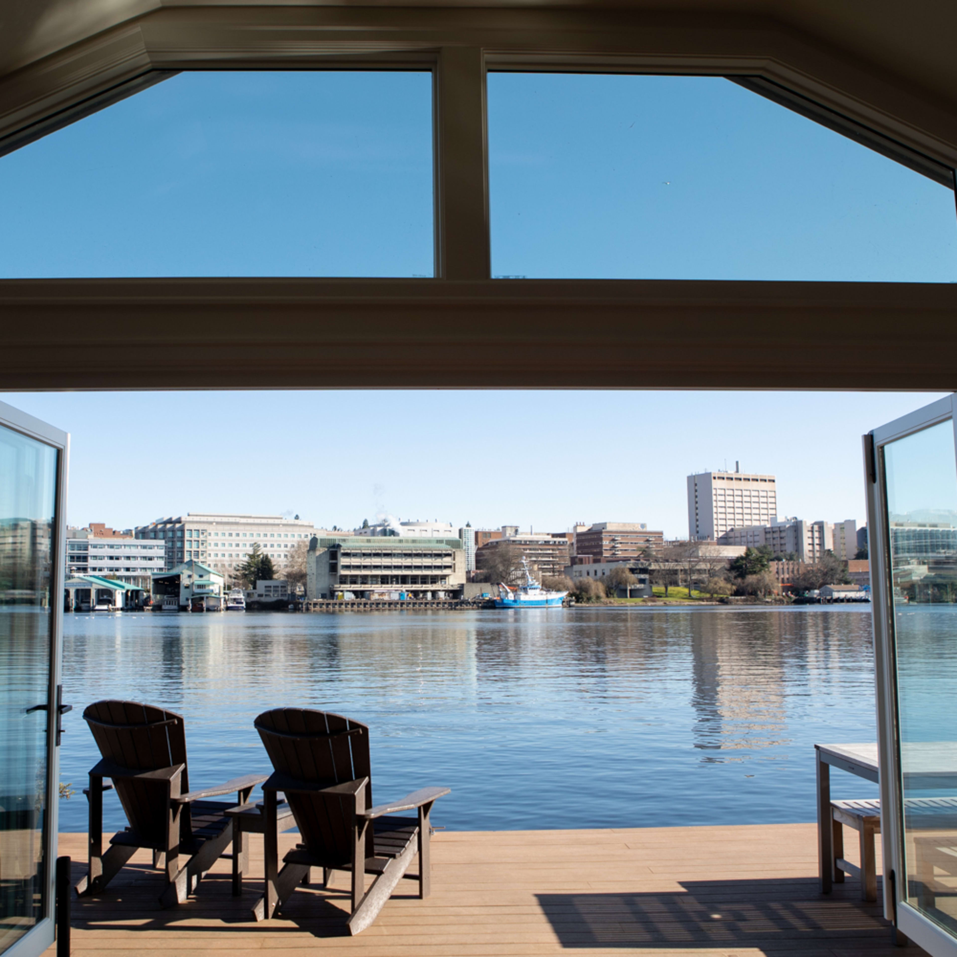 A view of a calm lake from a house, framed by open doors, with two chairs on a deck.