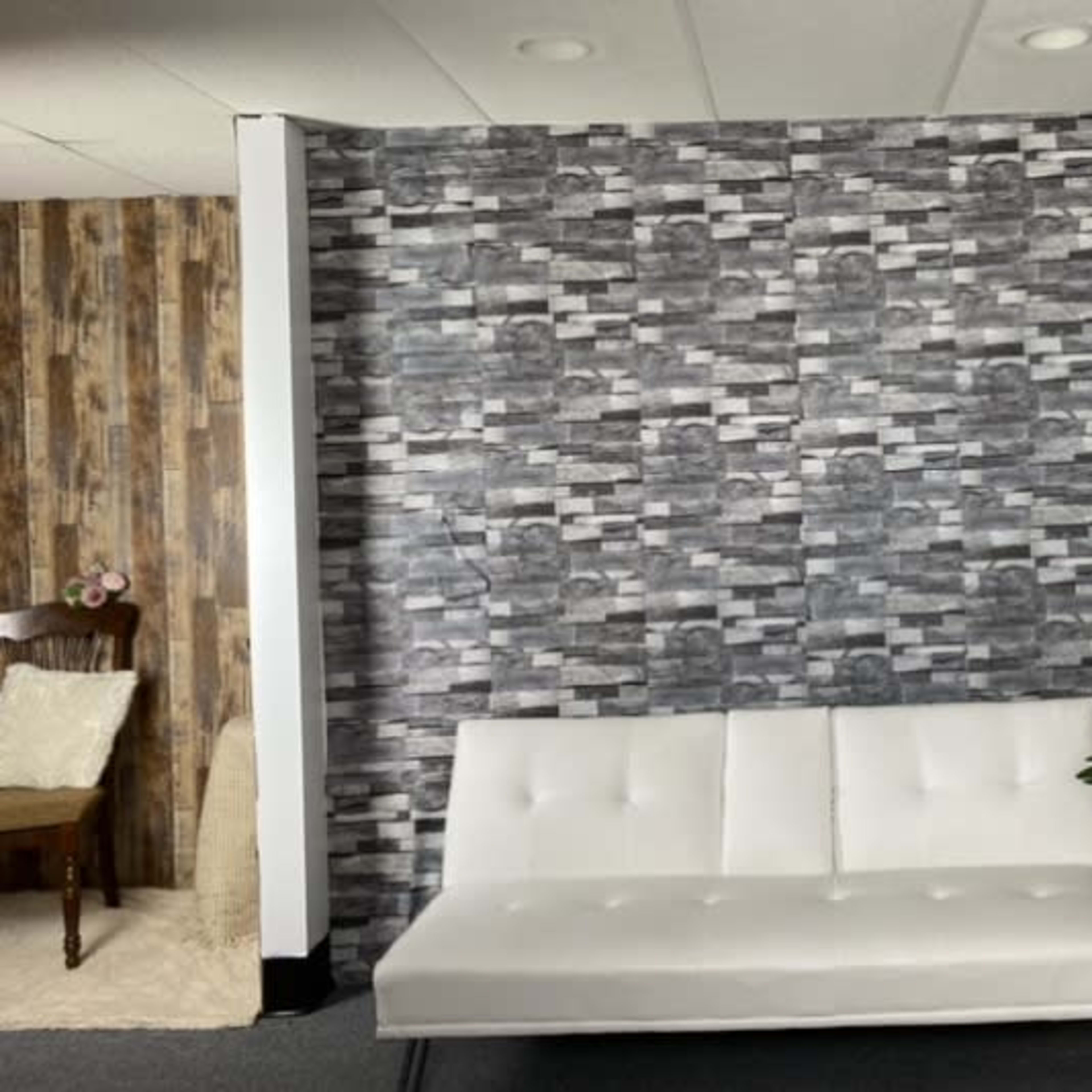 A sleek white futon against a patterned grey wall, with a newspaper-covered wall on one side and a potted plant nearby.