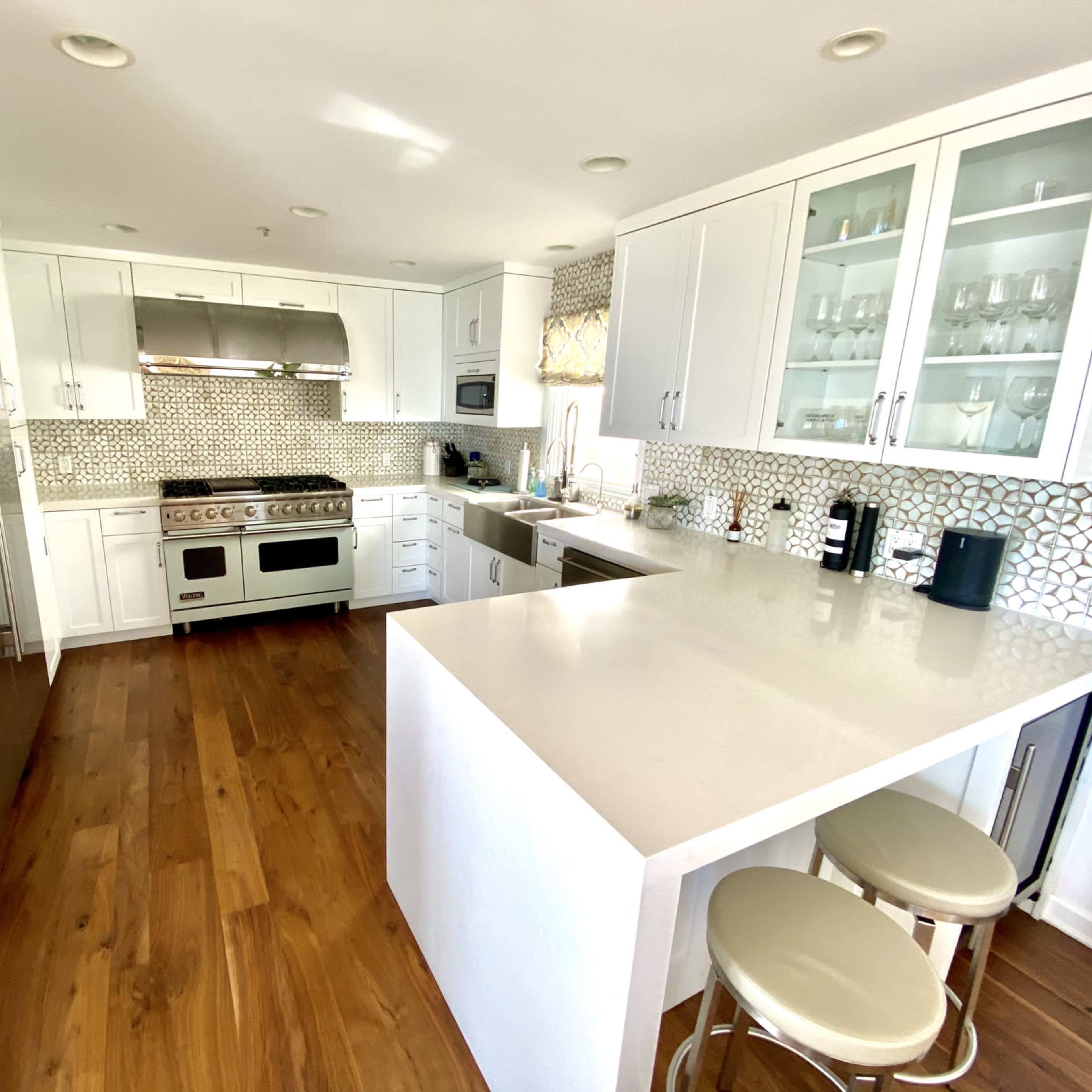 A modern kitchen featuring white cabinets, a large island with bar stools, and a backsplash made of geometric tiles.