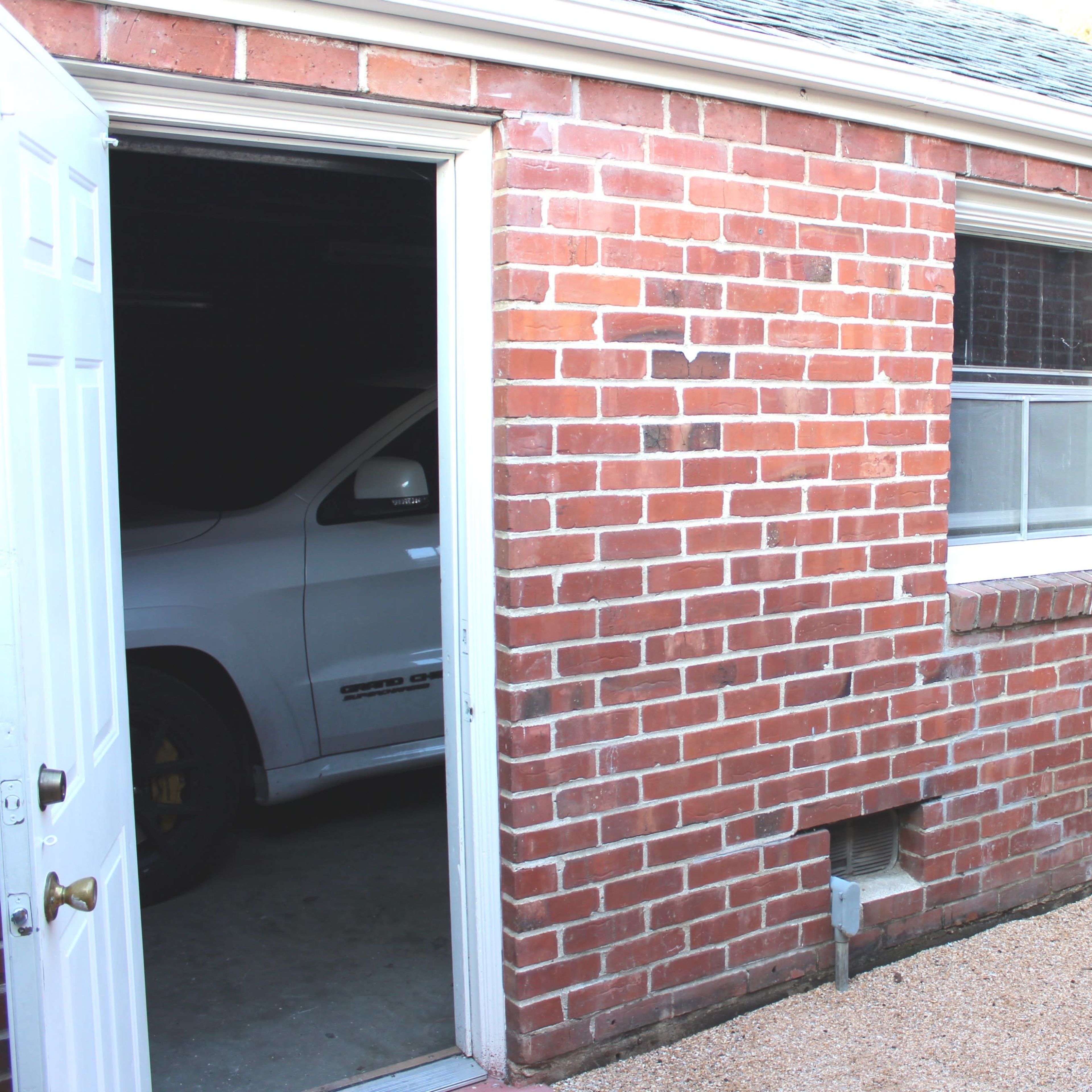 A brick exterior of a garage with an open door, revealing a vehicle partially visible inside.