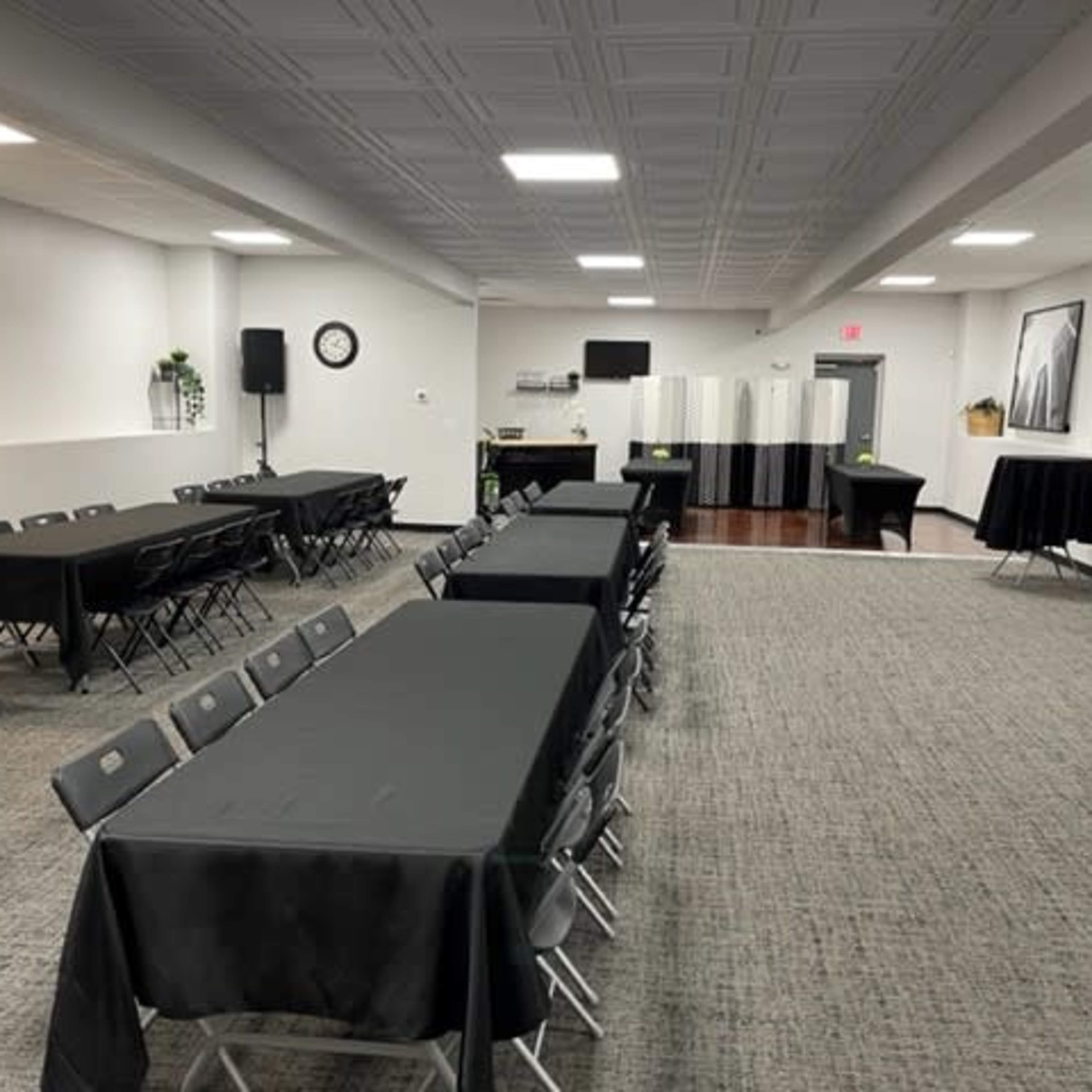 A large, empty event space with multiple black-covered tables arranged in rows and a few round tables set up along the perimeter.