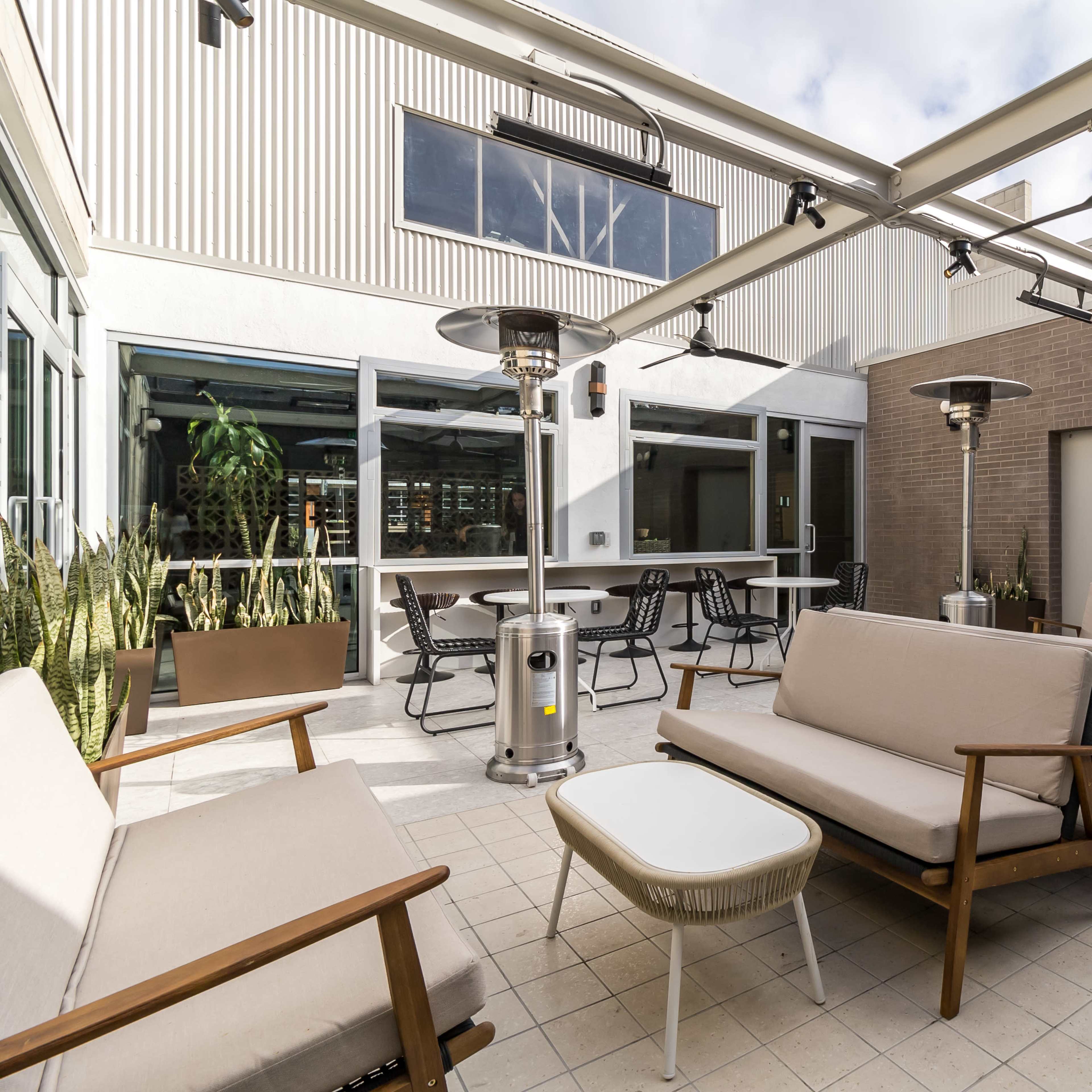 A spacious outdoor patio area with lounge seating, heating lamps, and a few potted plants.