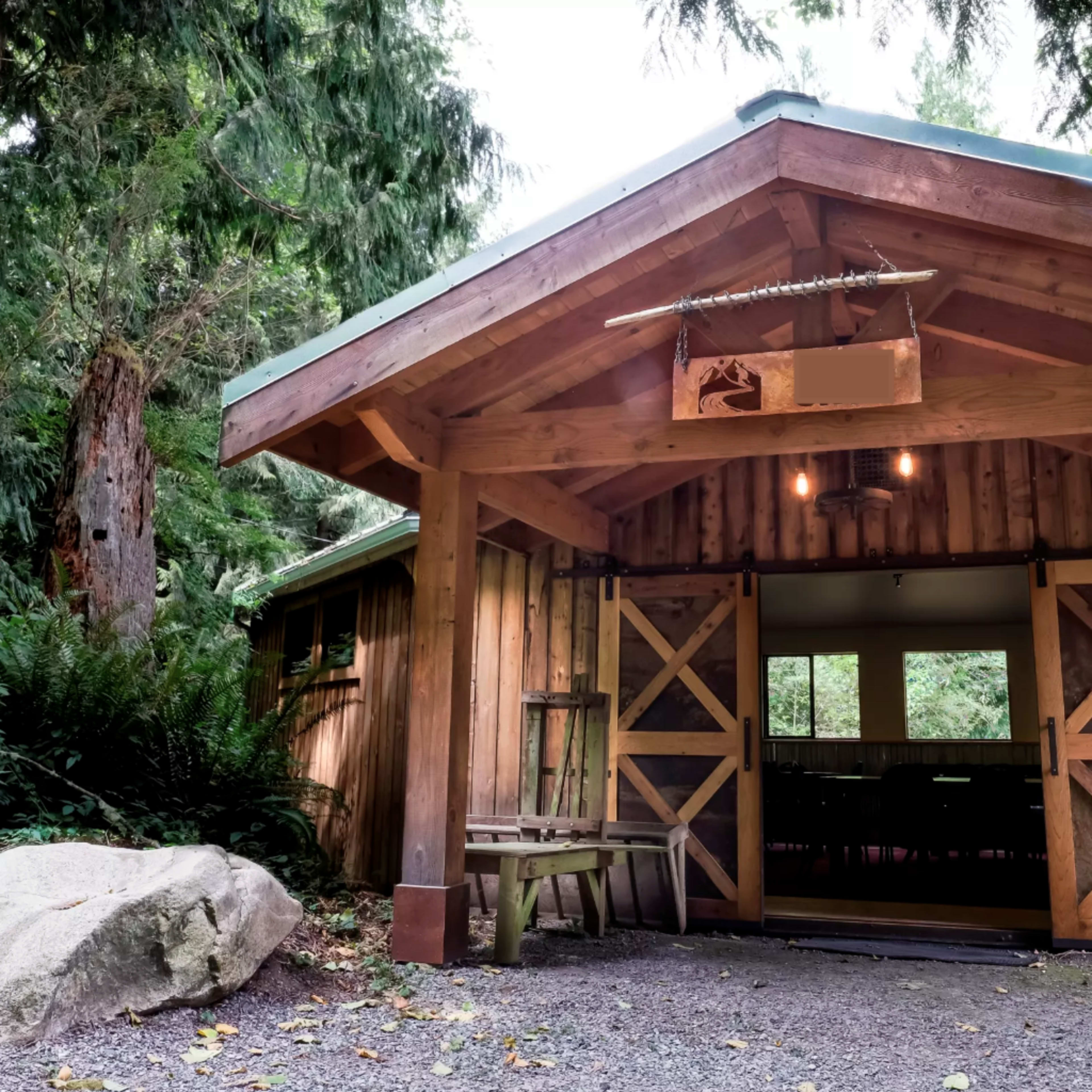 A rustic wooden entrance with a gabled roof leading into a cabin surrounded by trees and large rocks.