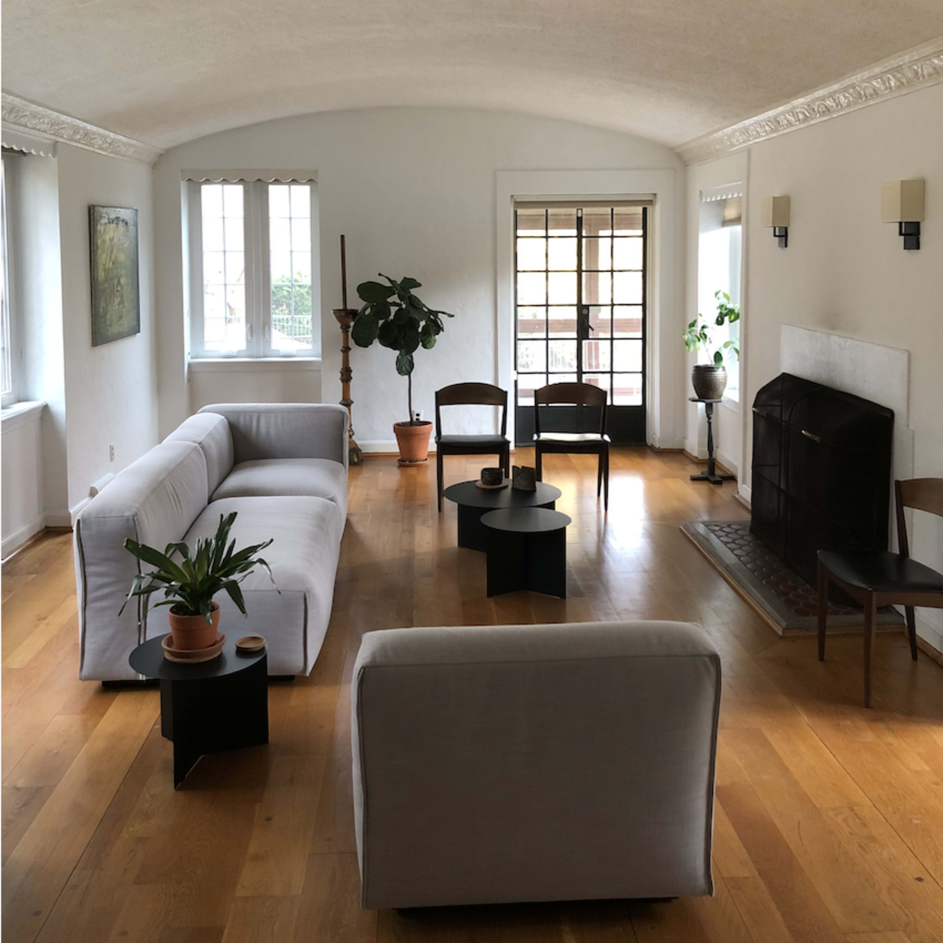 A spacious living room features a white sofa, two black chairs, a small table, and a fireplace, all arranged on polished wooden flooring.