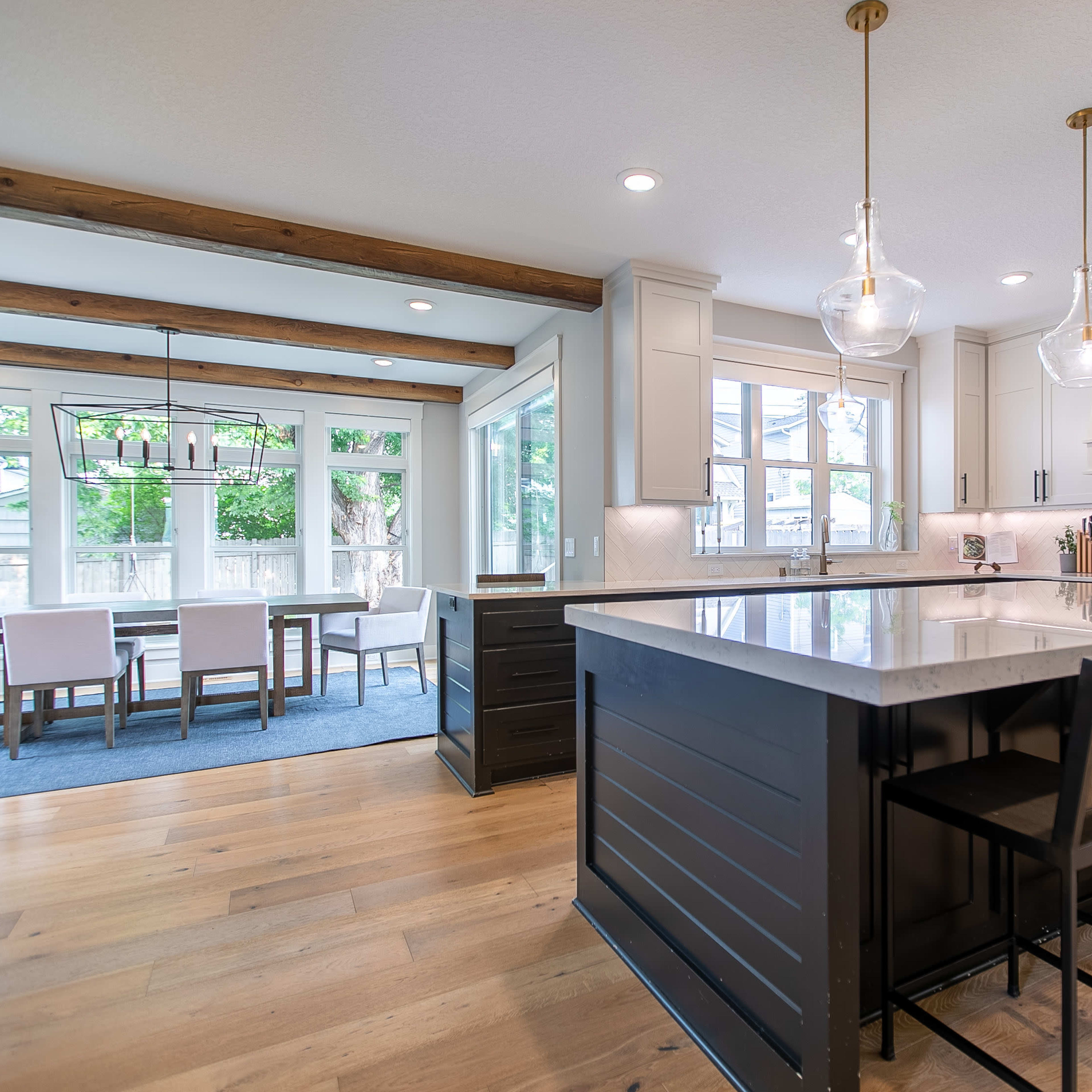 A modern kitchen features a large island with seating, white cabinetry, and a view of a dining area through large windows.