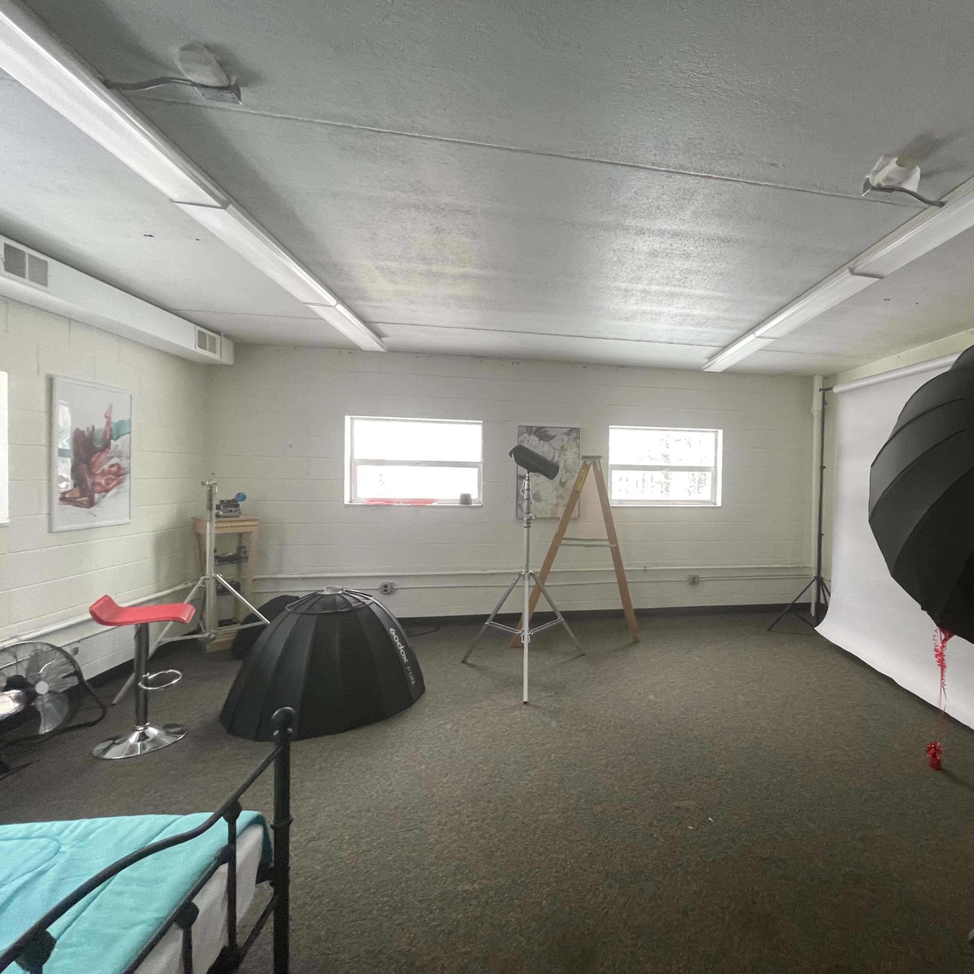 A photography studio with a backdrop, lighting equipment, a chair, and various props arranged in an empty, well-lit room.