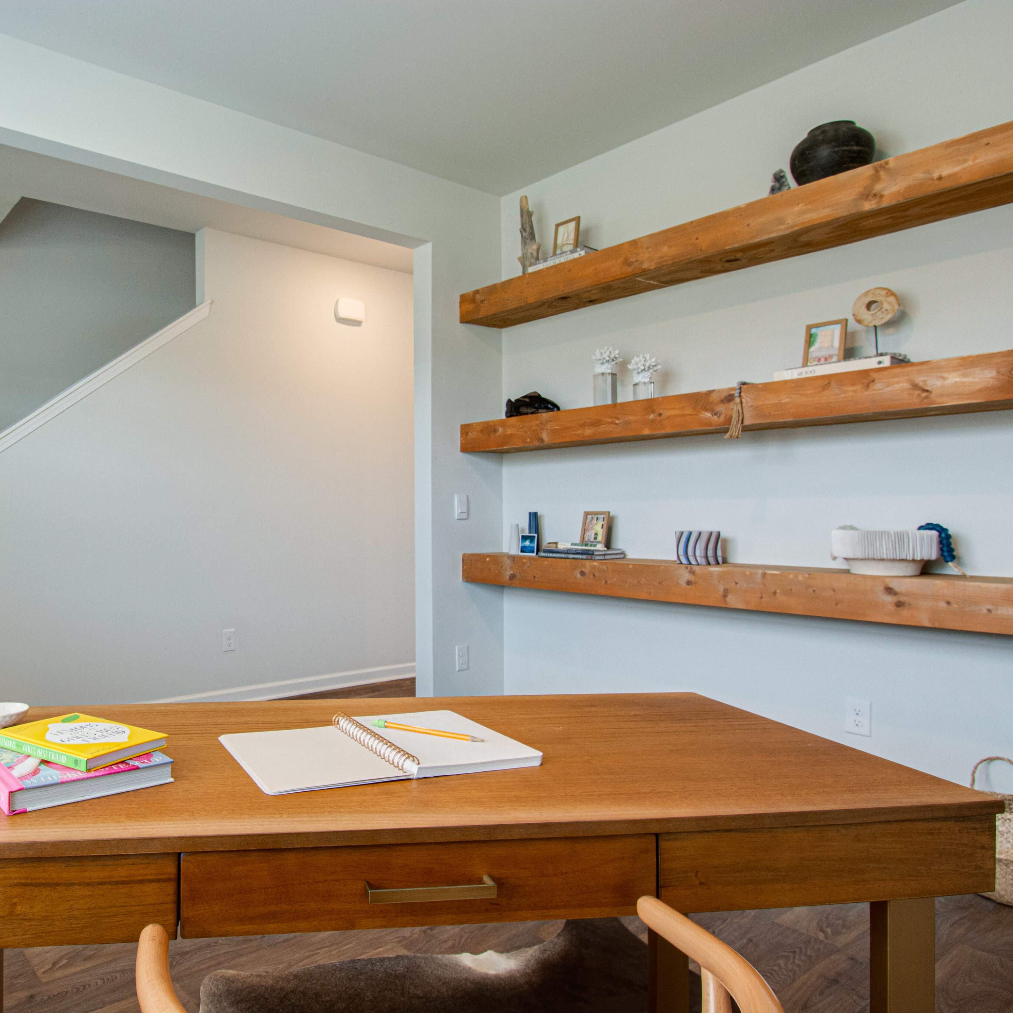 A home office with a wooden table, books on shelves, and a staircase in the background.
