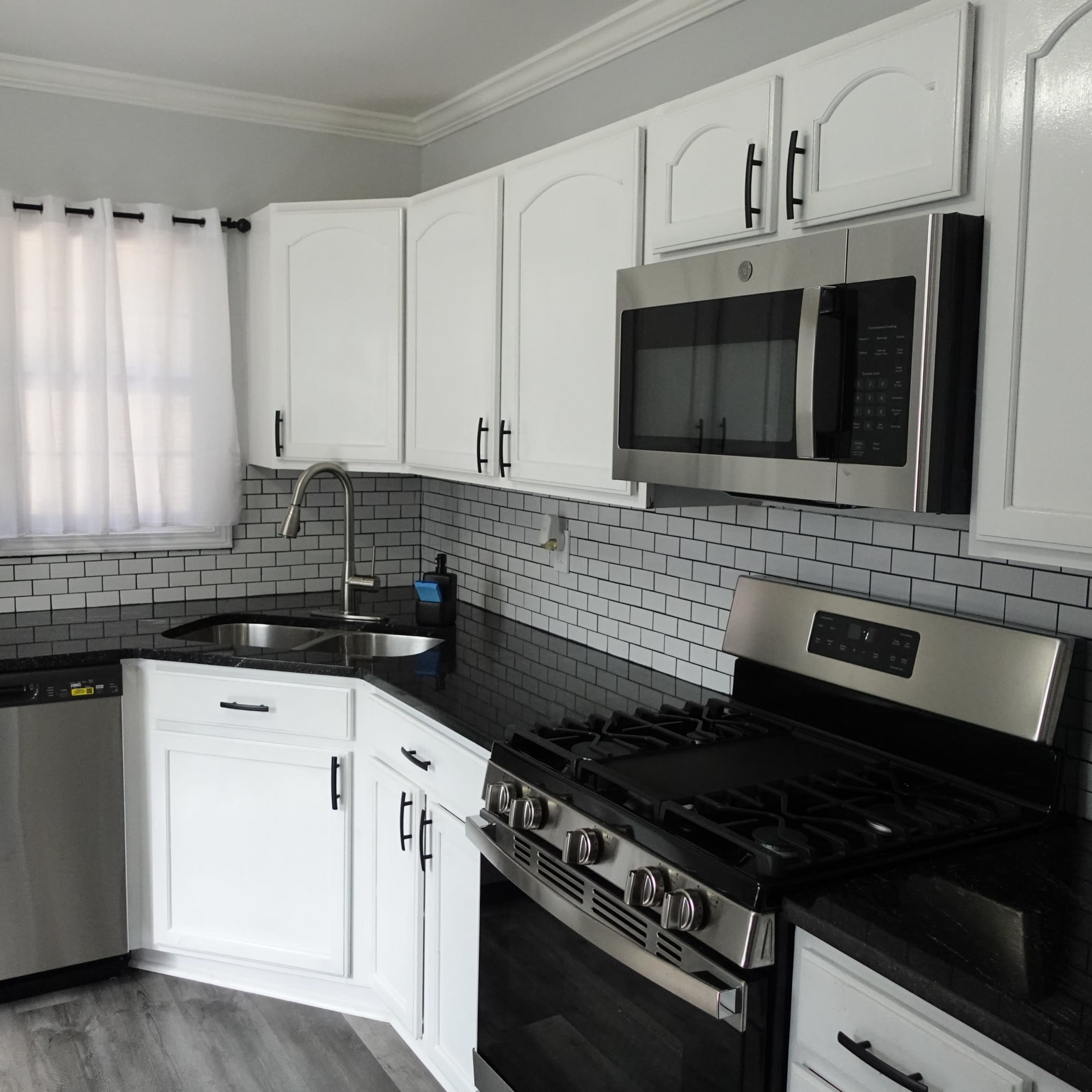 A modern kitchen with white cabinets, stainless steel appliances, a black granite countertop, and a tiled backsplash.
