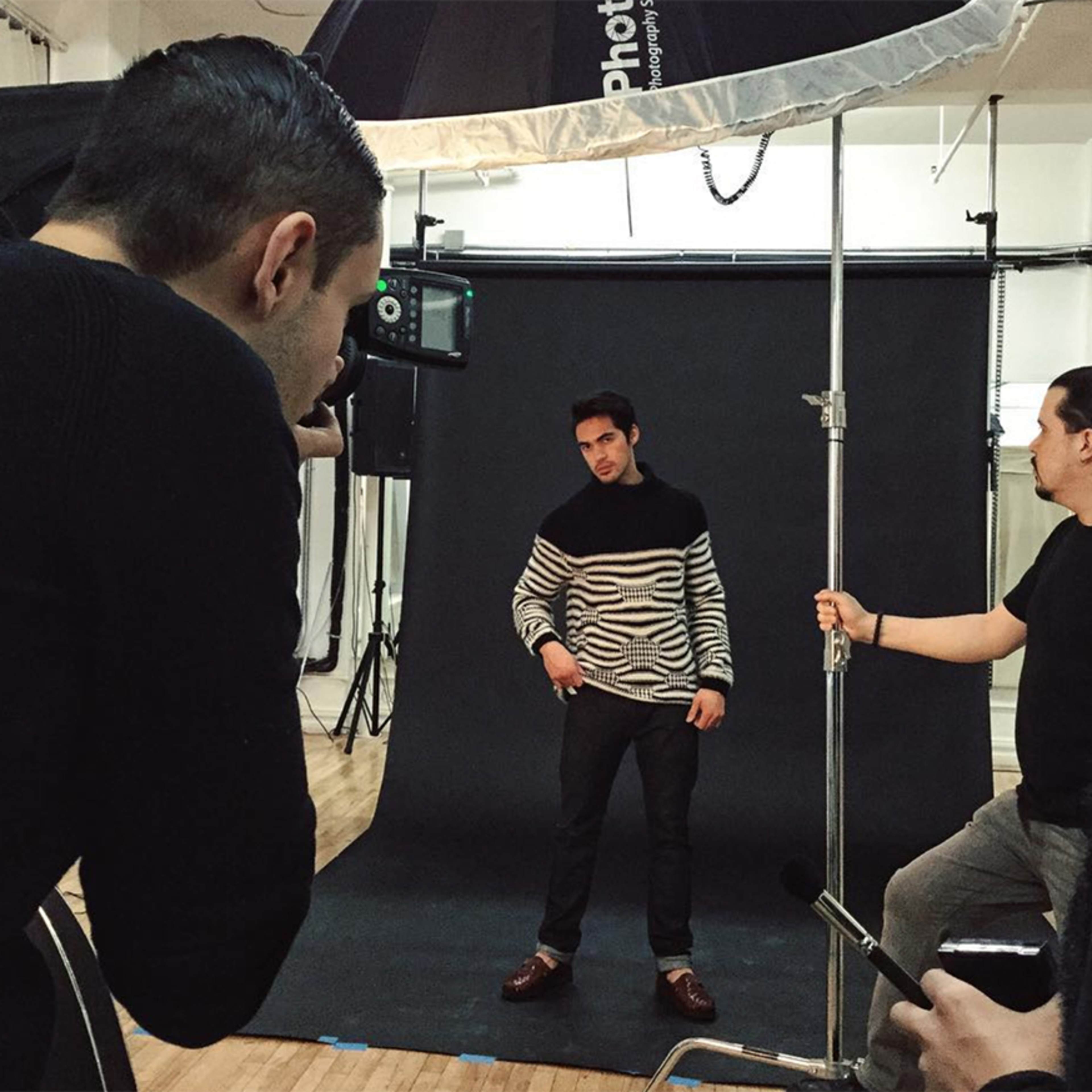 A photographer is capturing a model posing against a black backdrop in a studio setting.