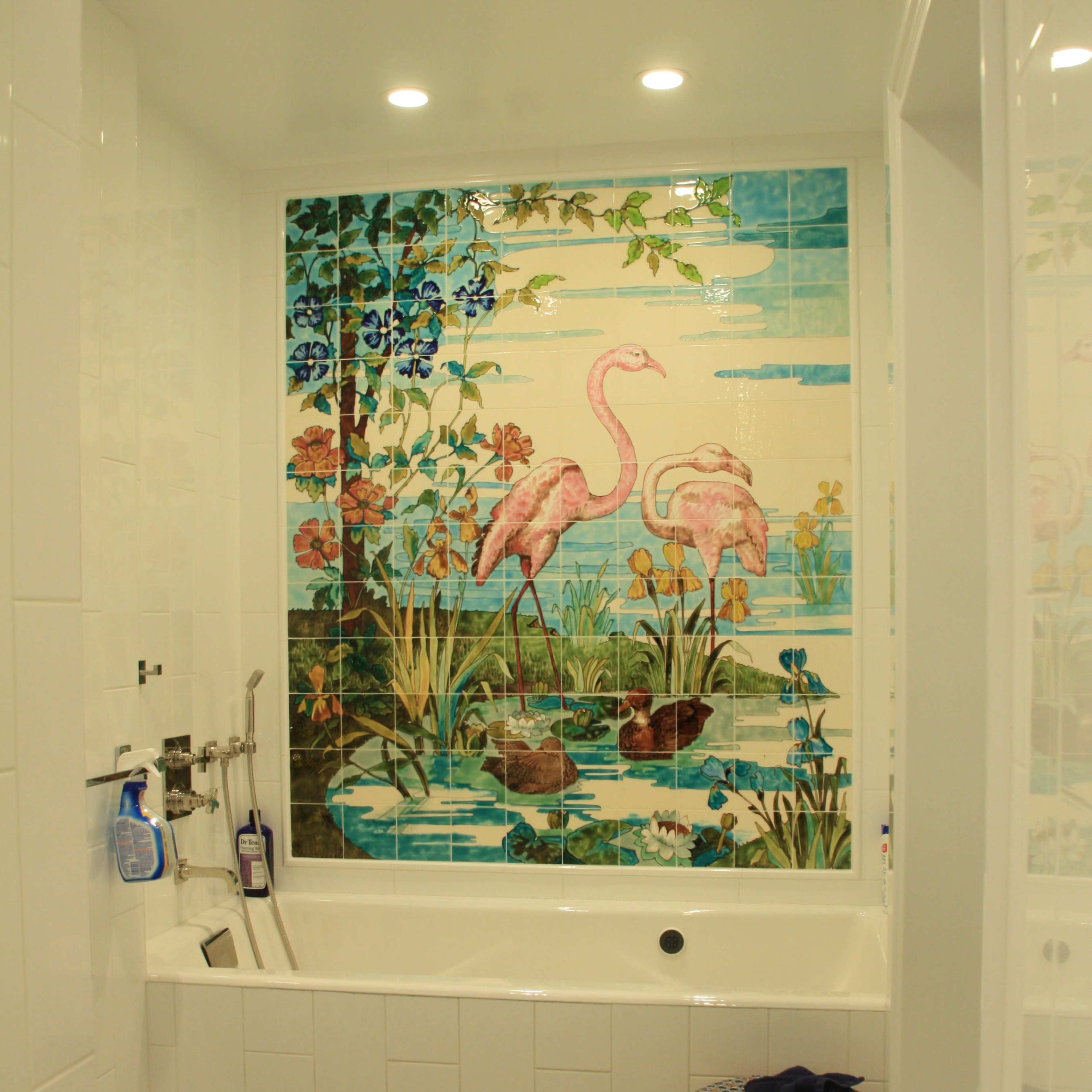 The bathroom features a large tiled mural of flamingos surrounded by greenery above a bathtub, with a shower area and a small stool nearby.