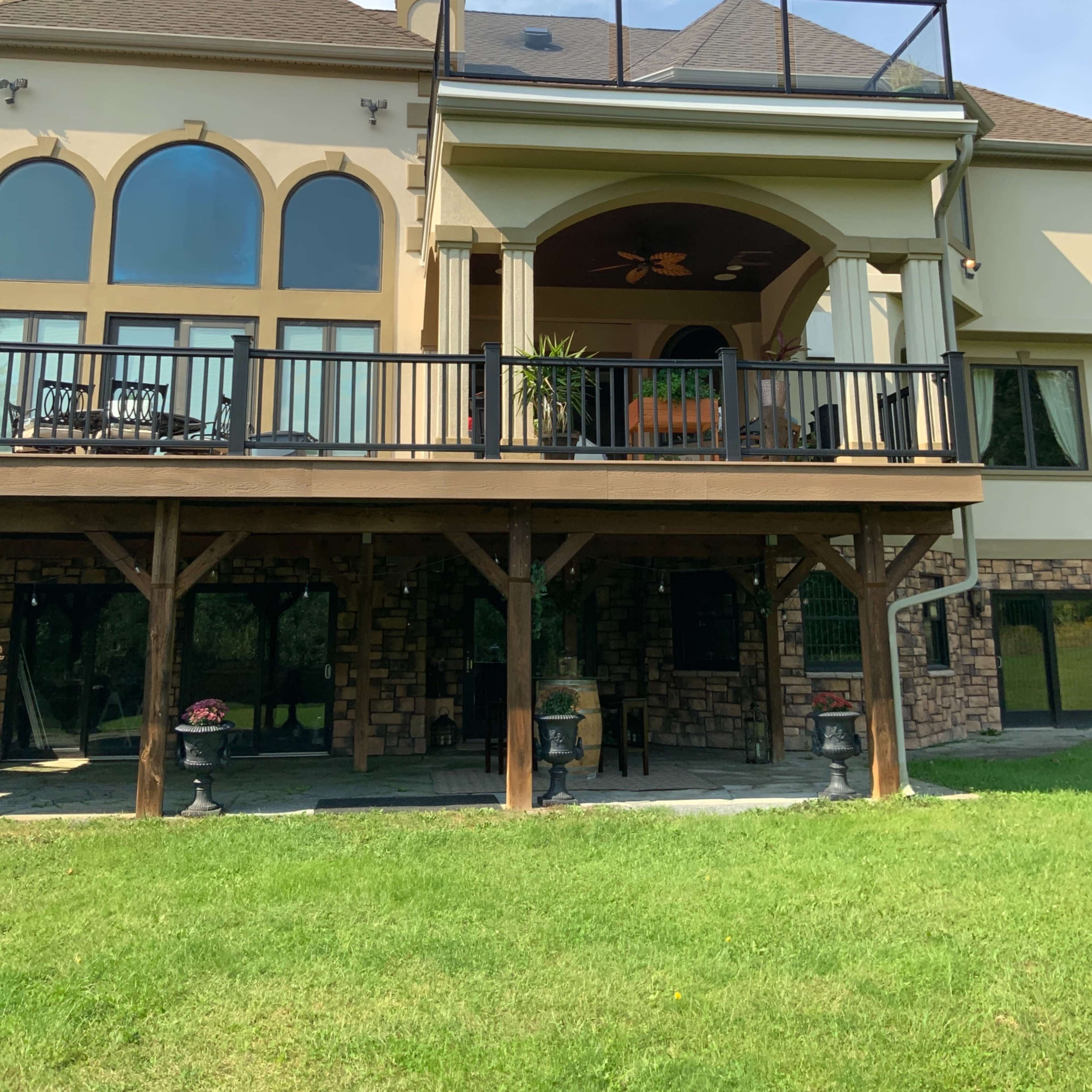 A multi-level house with a large deck supported by wooden posts and a balcony featuring large arched windows.