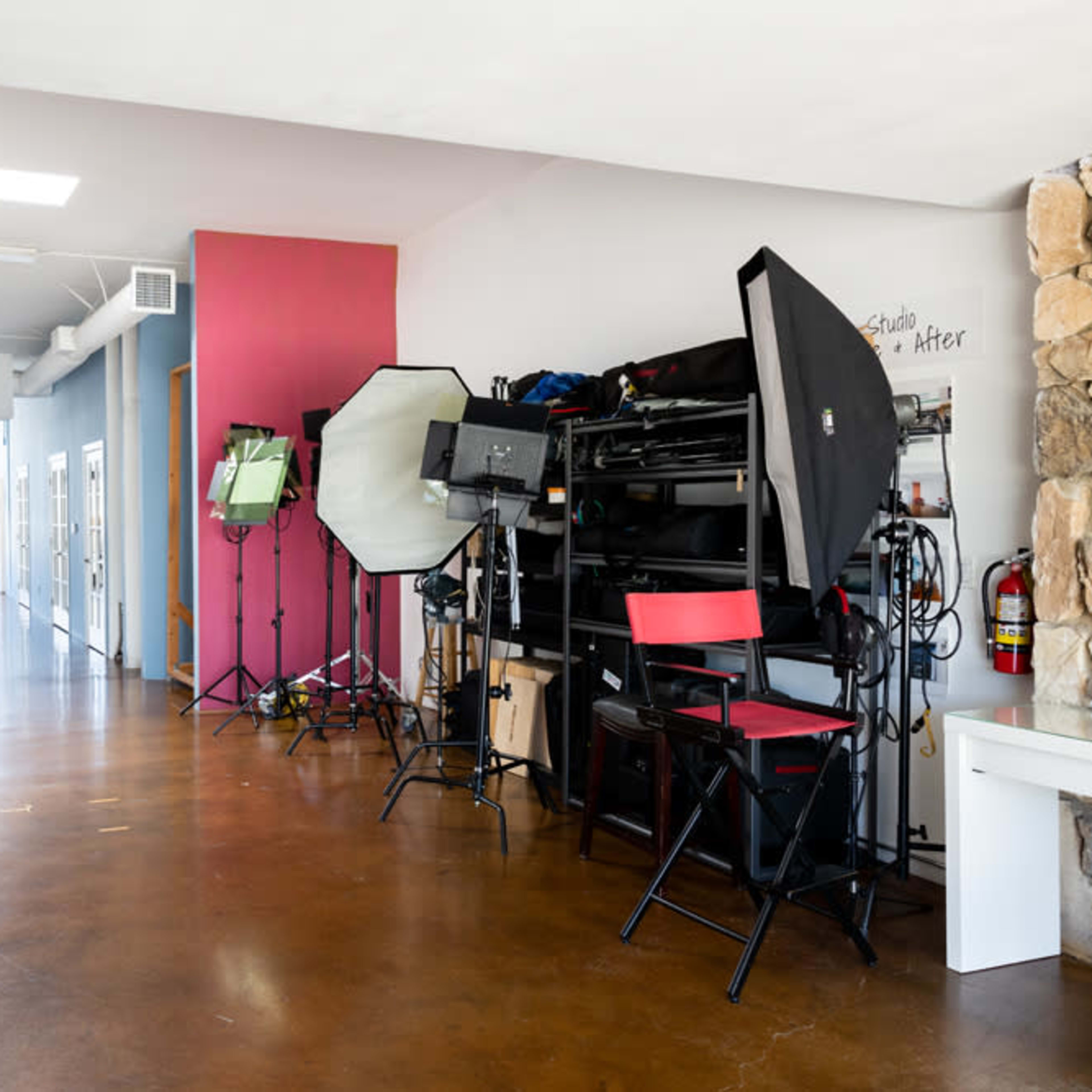 A spacious hallway features multiple photography equipment stands, backdrops, and a variety of lighting setups along one side, with a clear pathway leading to an entrance at the far end.