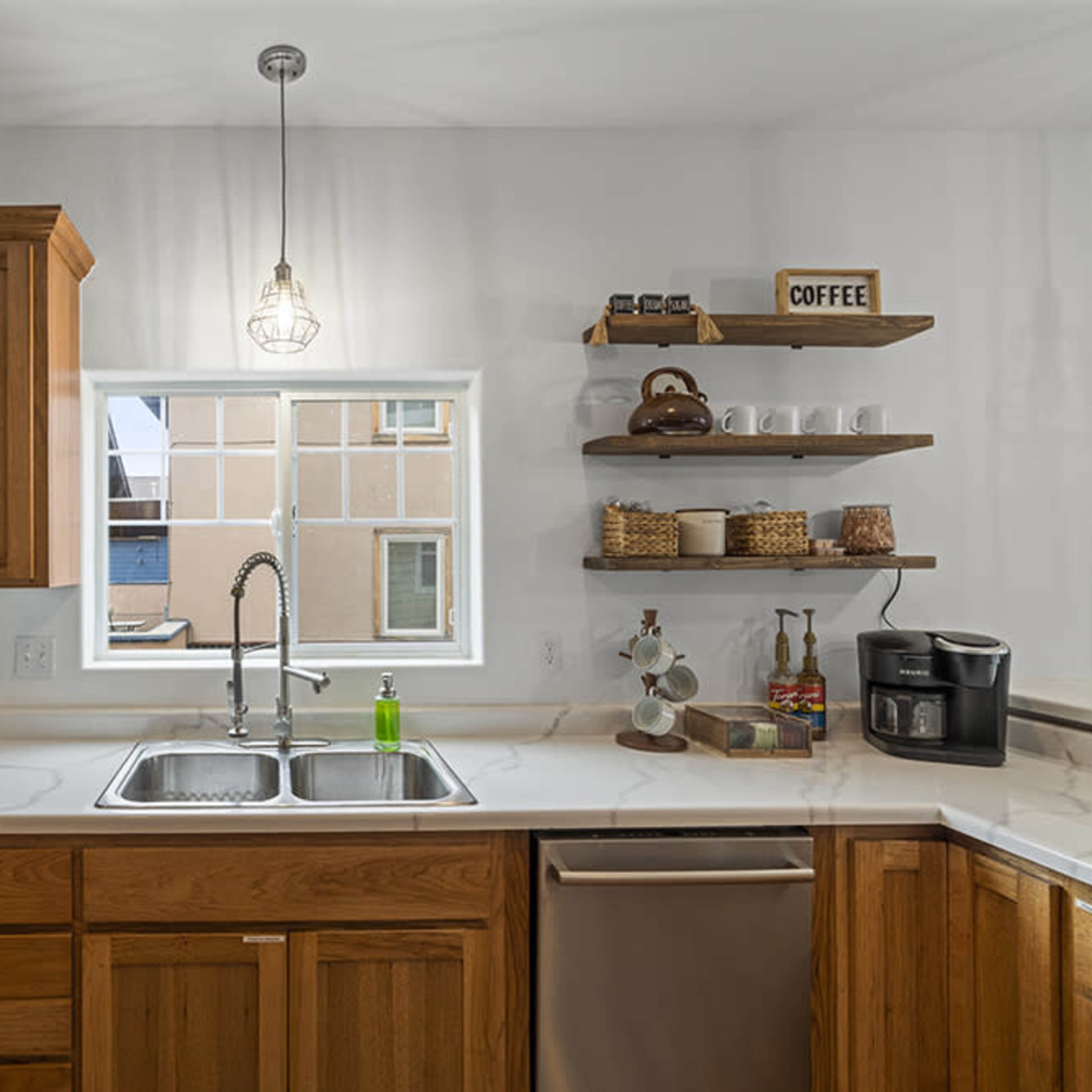 A modern kitchen features wooden cabinetry, a double sink, and open shelves displaying coffee-related items near a window.