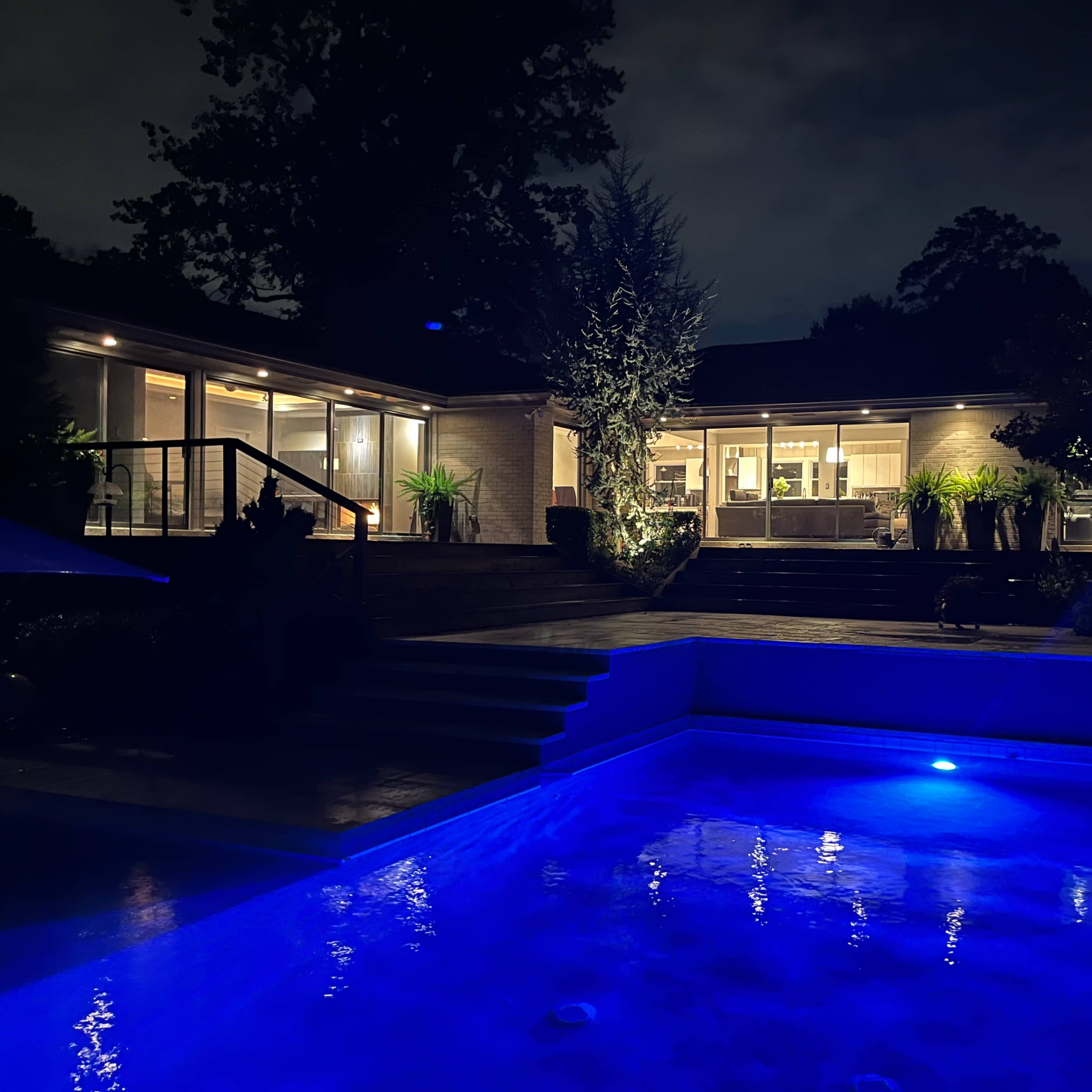A well-lit house at night with a pool illuminated by blue lights in the foreground.