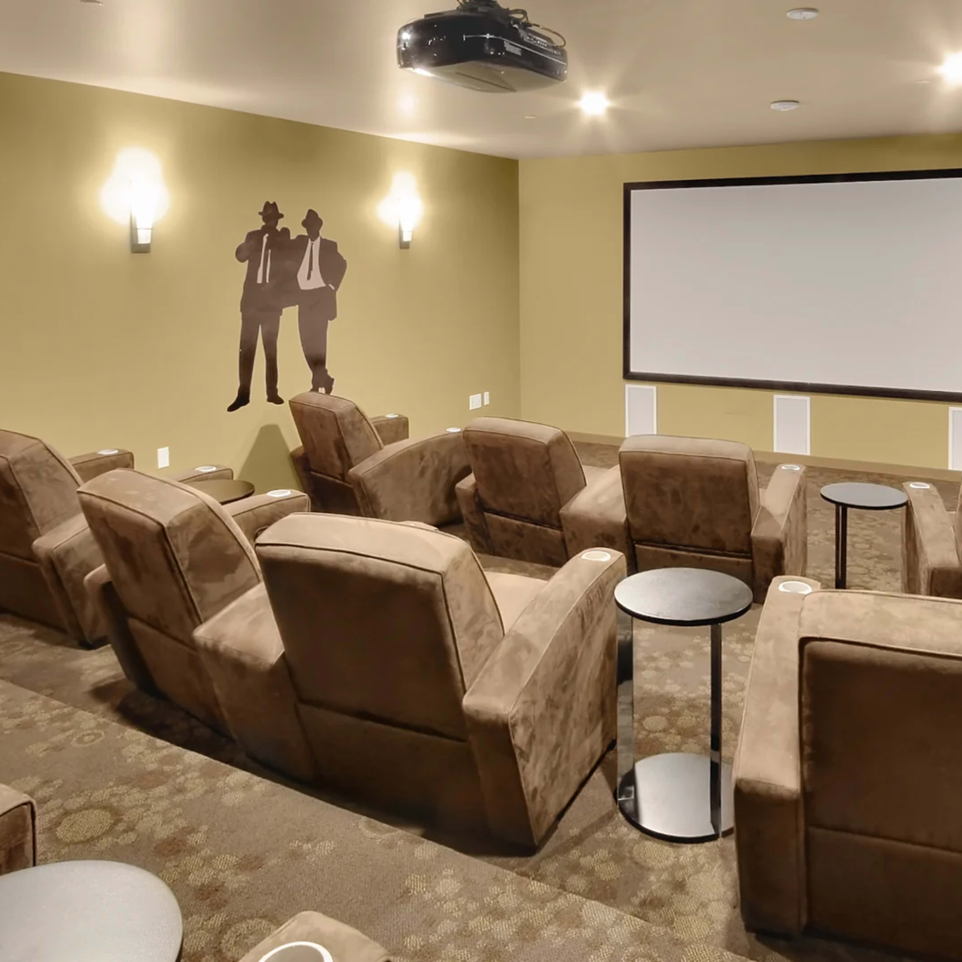 A small home theater room with plush seating, a large screen, and projector mounted on the ceiling.