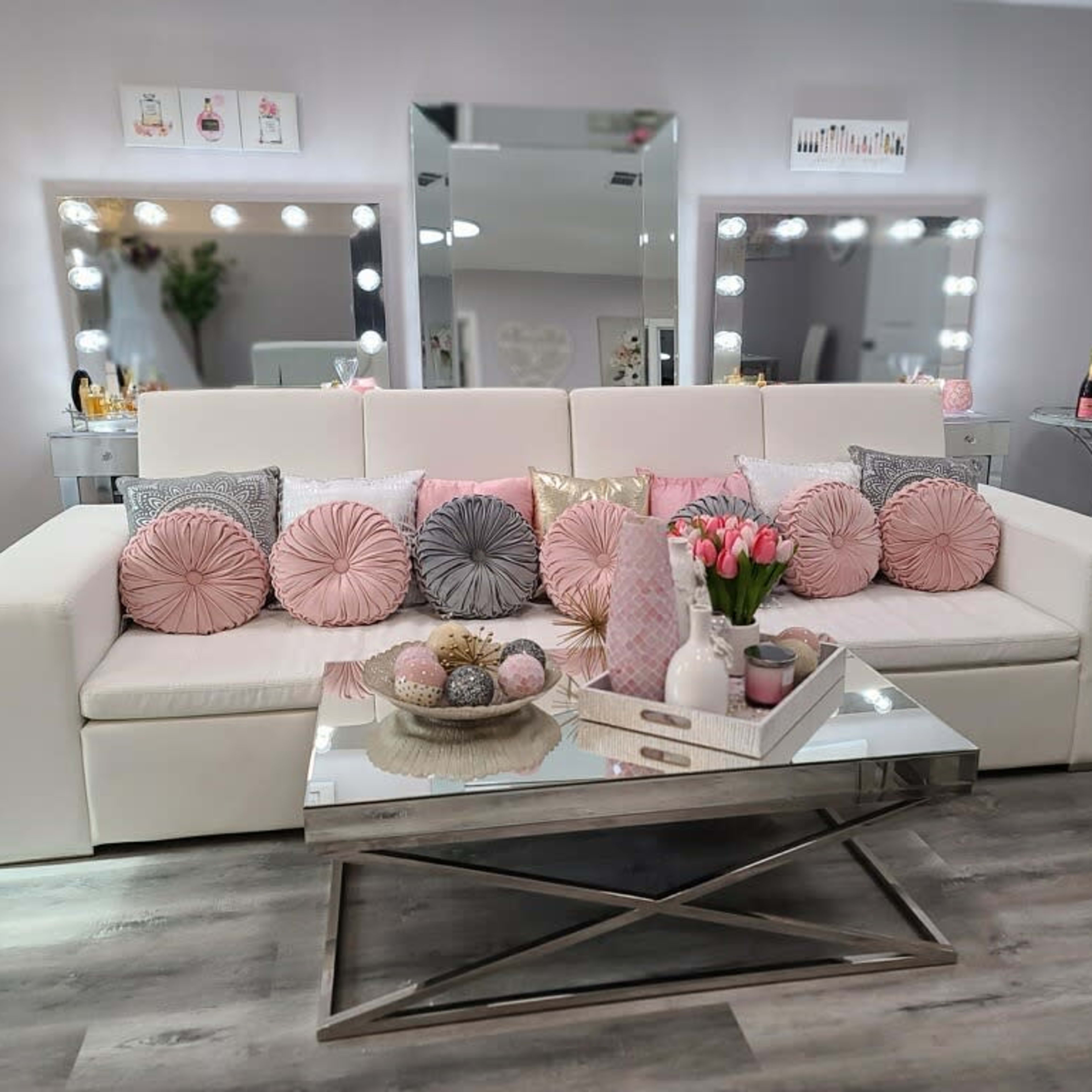 A modern living room with a white sofa adorned with decorative pillows, a glass coffee table in front, and mirrors reflecting the space.
