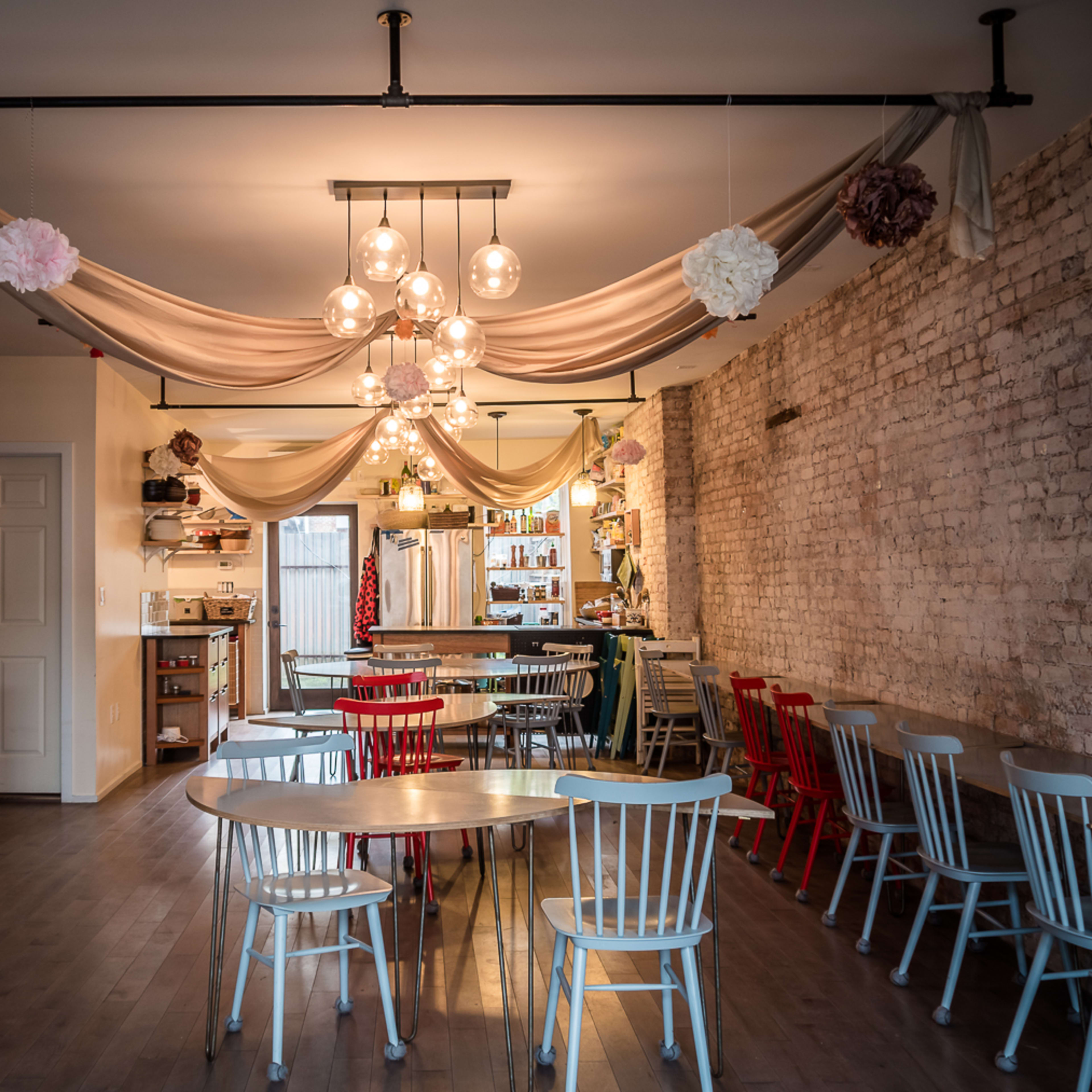 A cozy café interior featuring wooden tables and colorful chairs arranged under decorative drapes and pendant lighting.