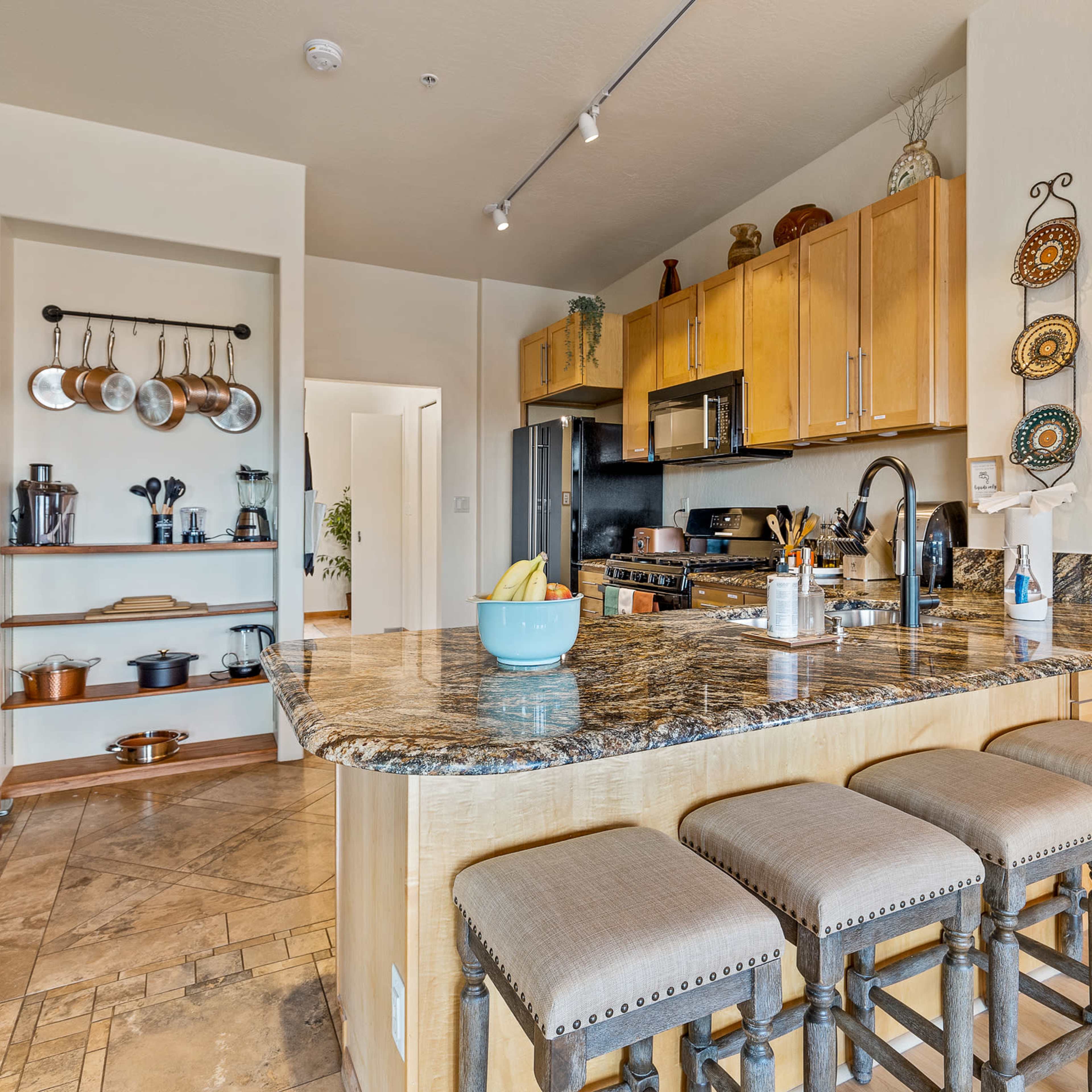 A modern kitchen with wooden cabinets, granite countertops, and a central island with barstools.