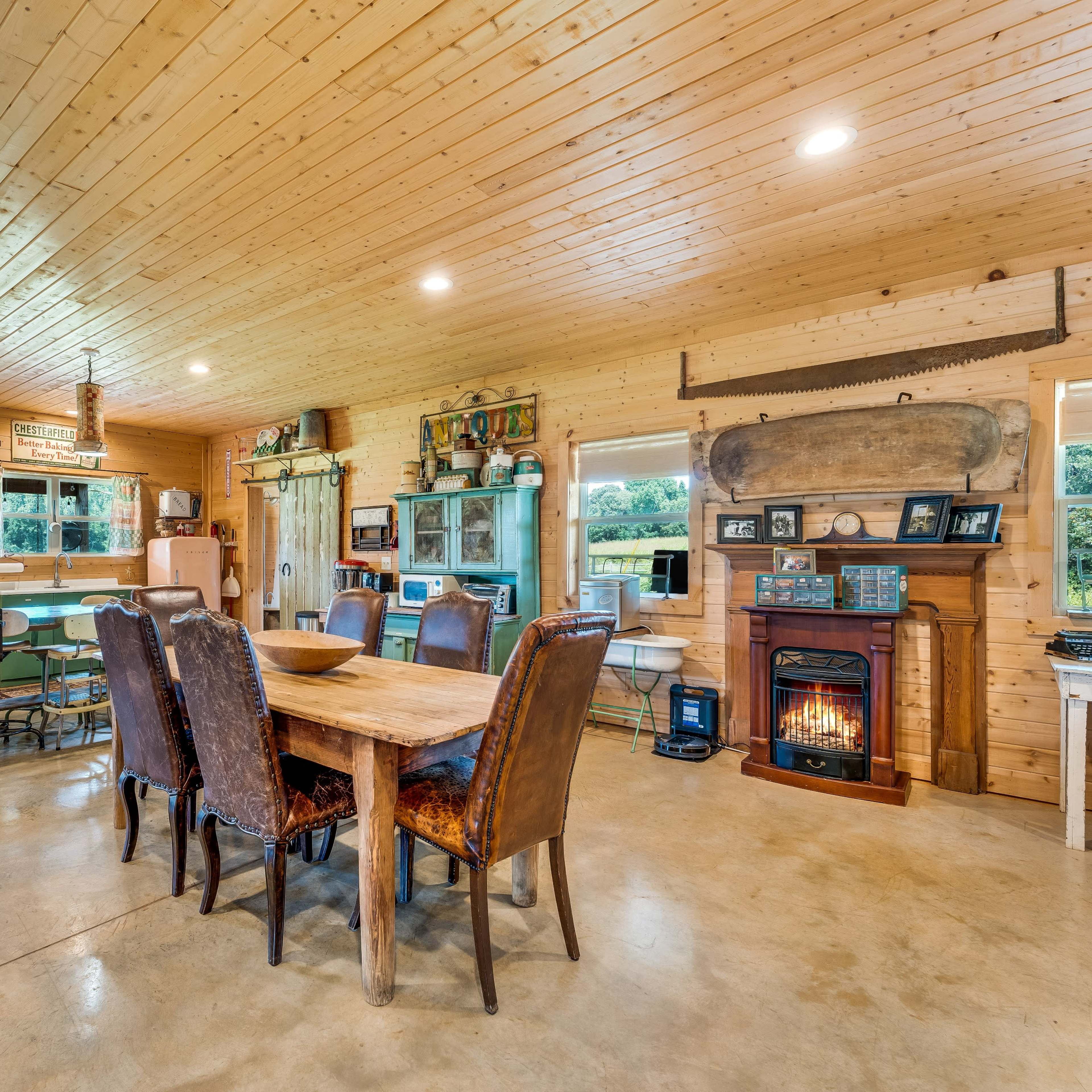 A spacious, rustic kitchen and dining area with wooden walls, a large dining table, and a cozy fireplace.