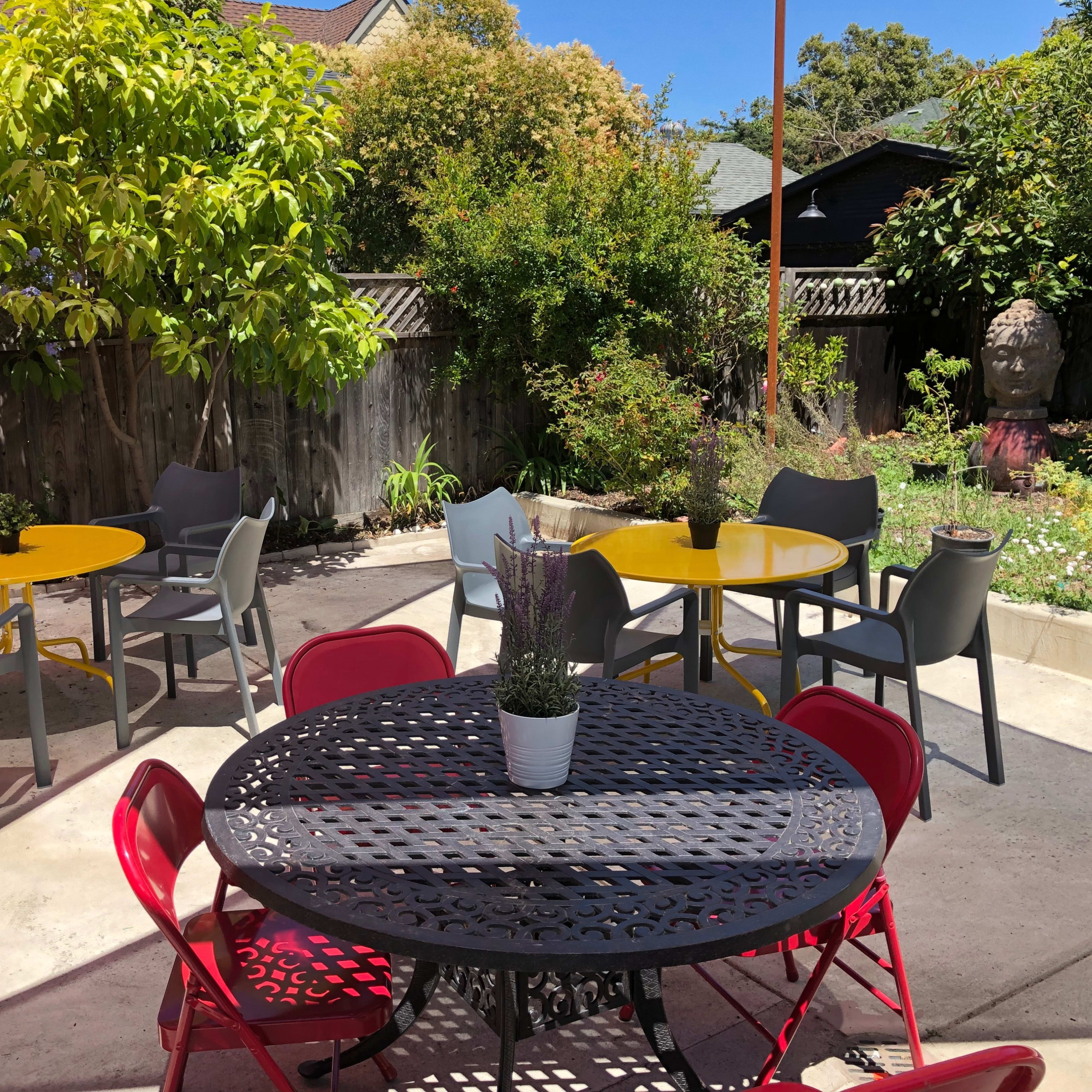 A outdoor seating area features several tables in yellow and black, surrounded by greenery and colorful chairs.
