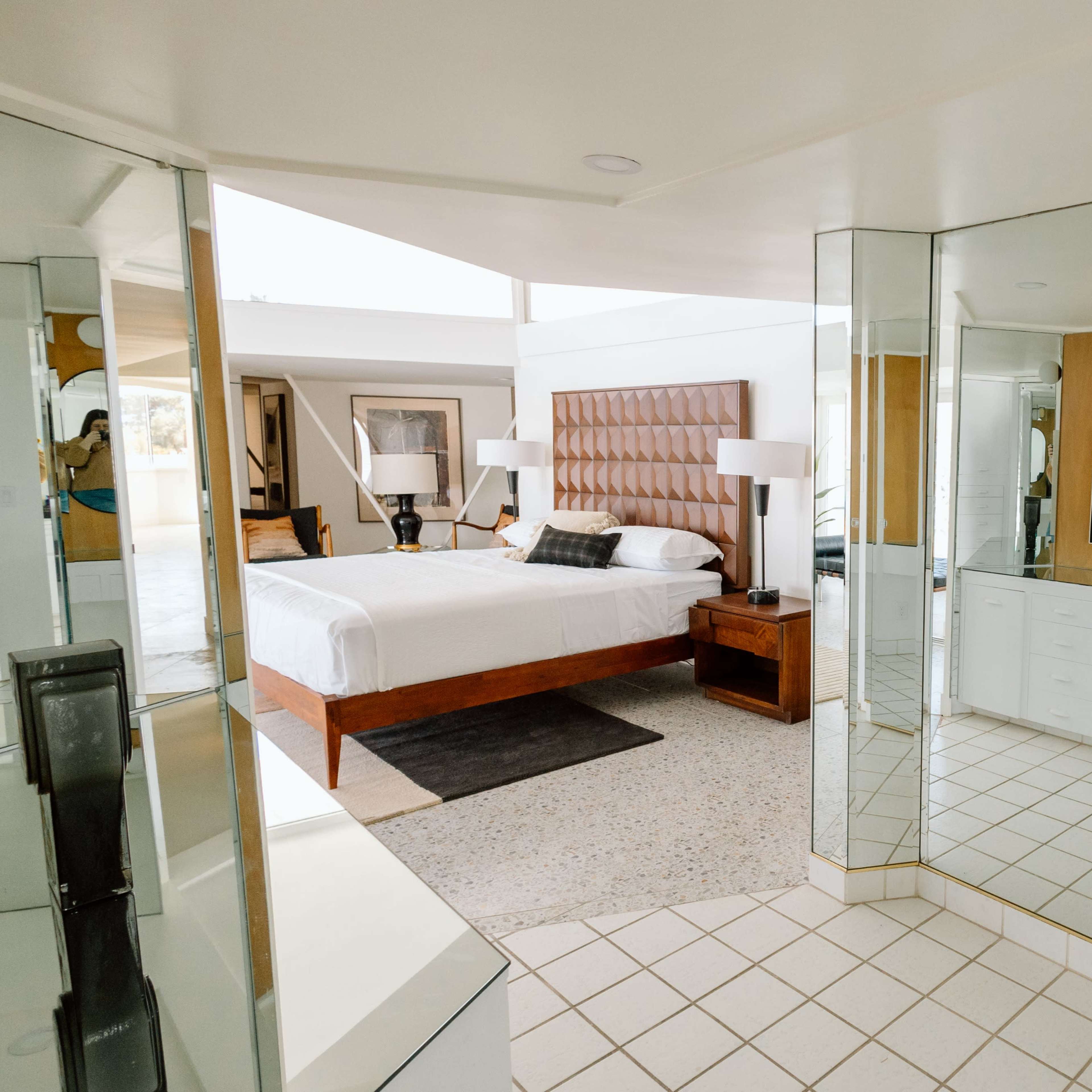 A modern bedroom with a mirrored wall, a king-sized bed, and a sleek vanity area.