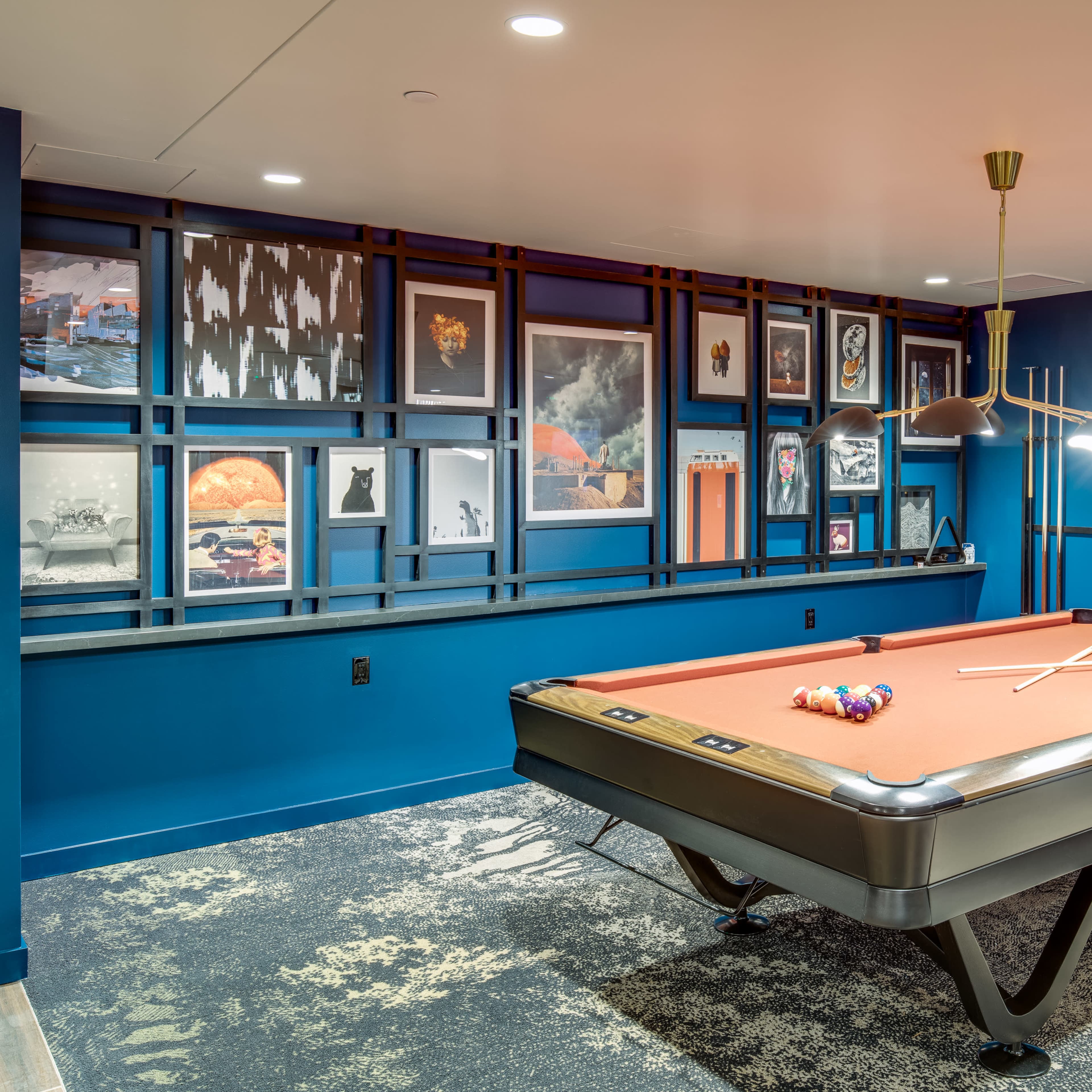A pool table in a room with blue walls and a gallery of framed artwork on the adjacent wall.