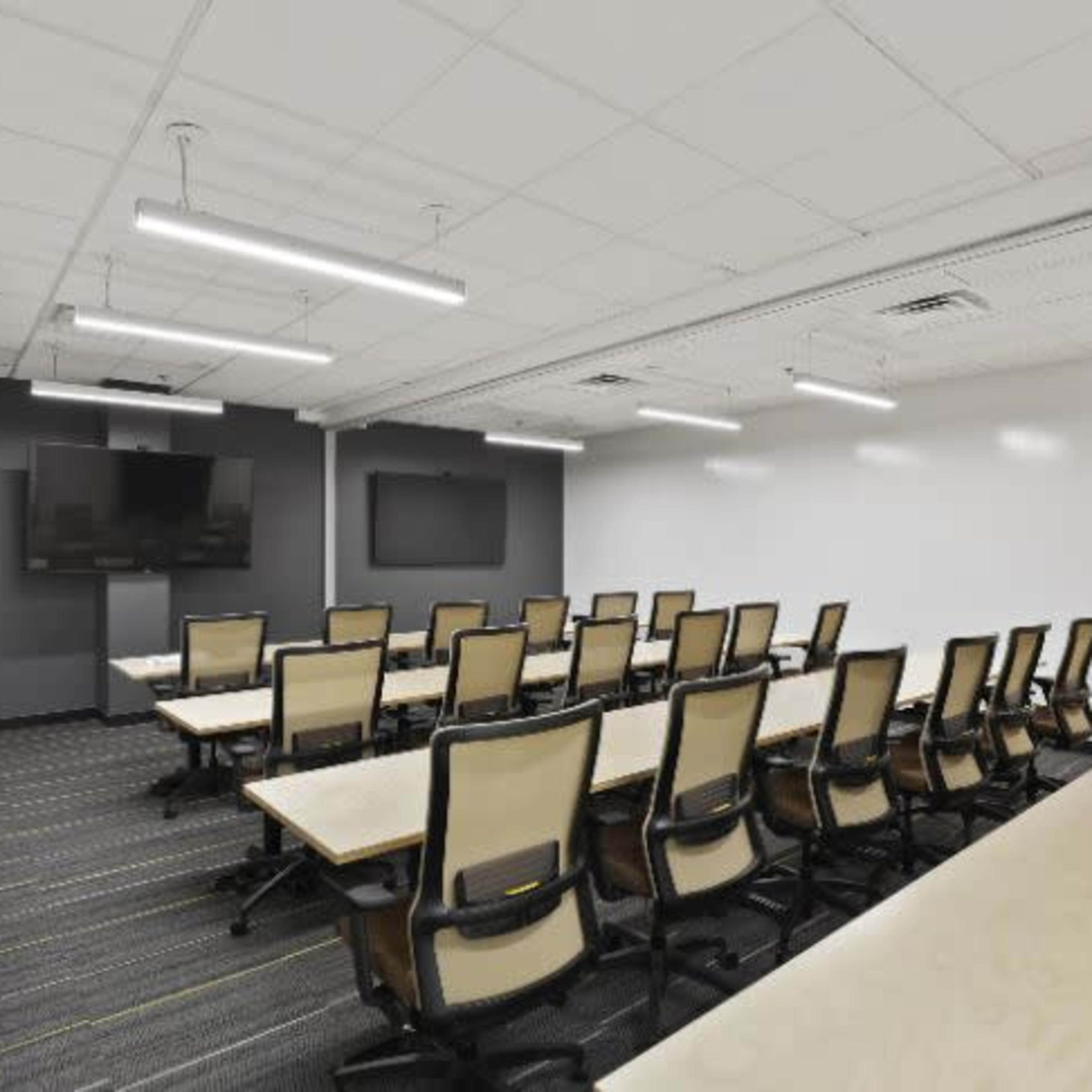 A modern conference room features rows of chairs facing two wall-mounted screens.