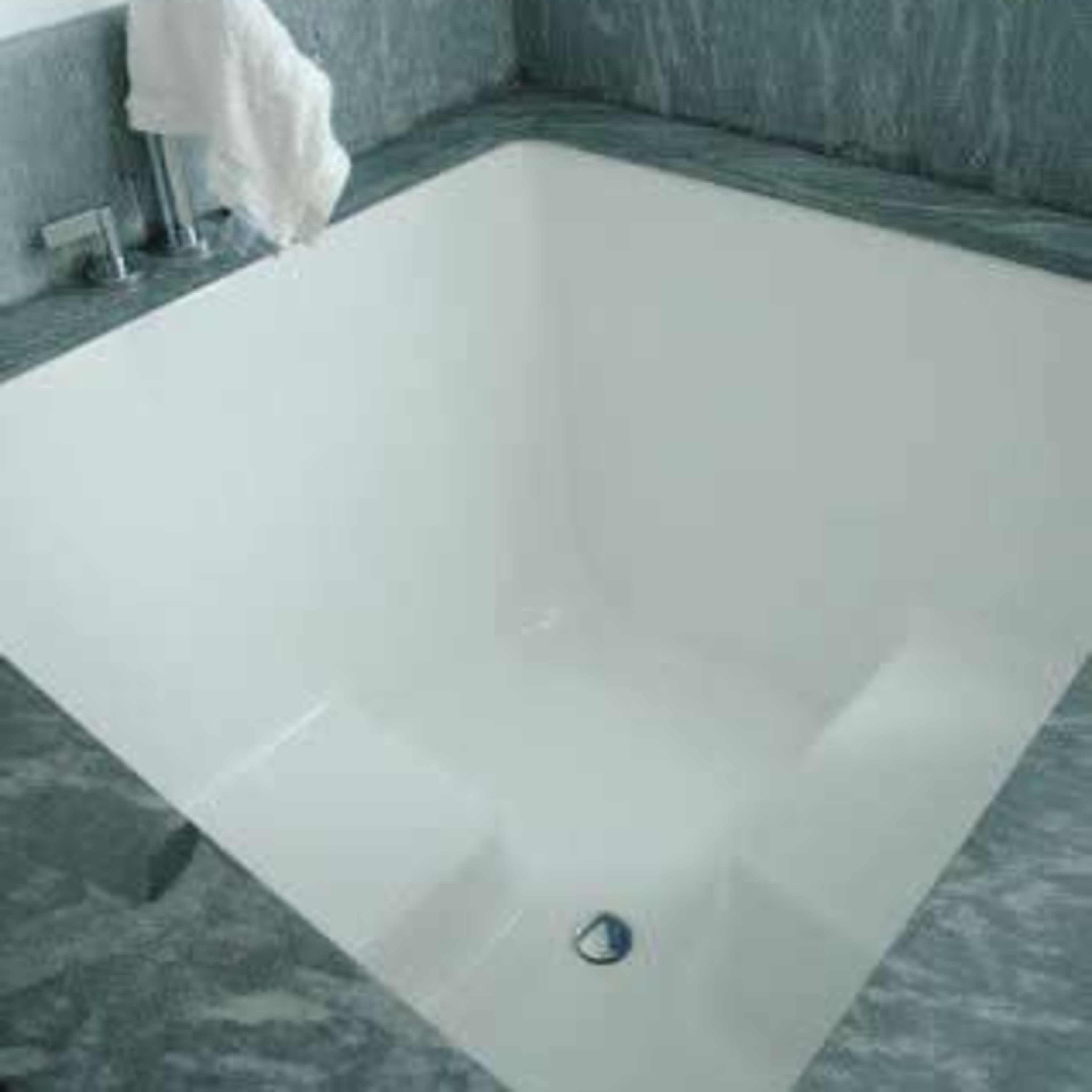 A square bathtub with a sleek white finish and marble surrounding, positioned against a wall with blue tiles.