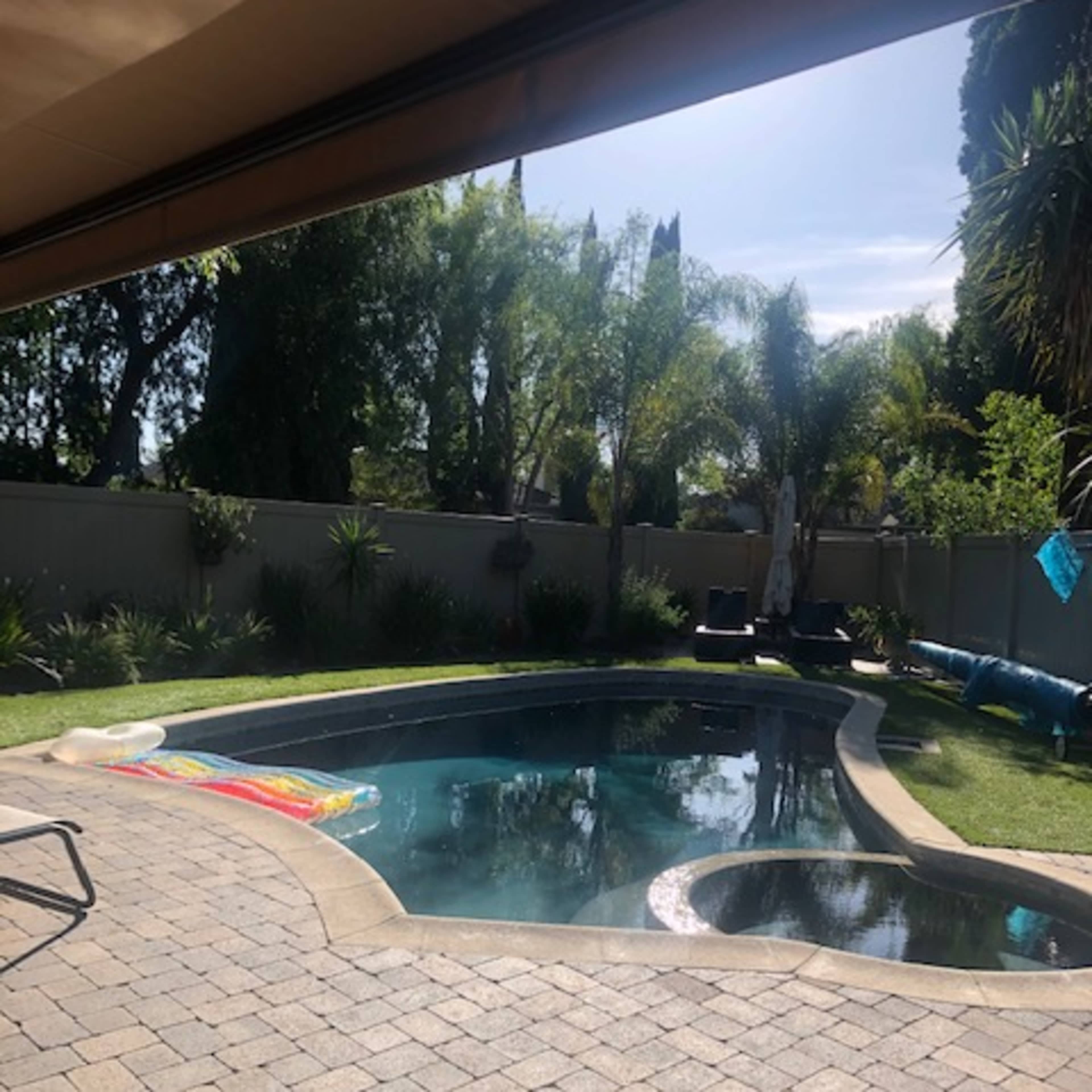 A swimming pool with a slide is surrounded by landscaped greenery and a patio area made of pavers.