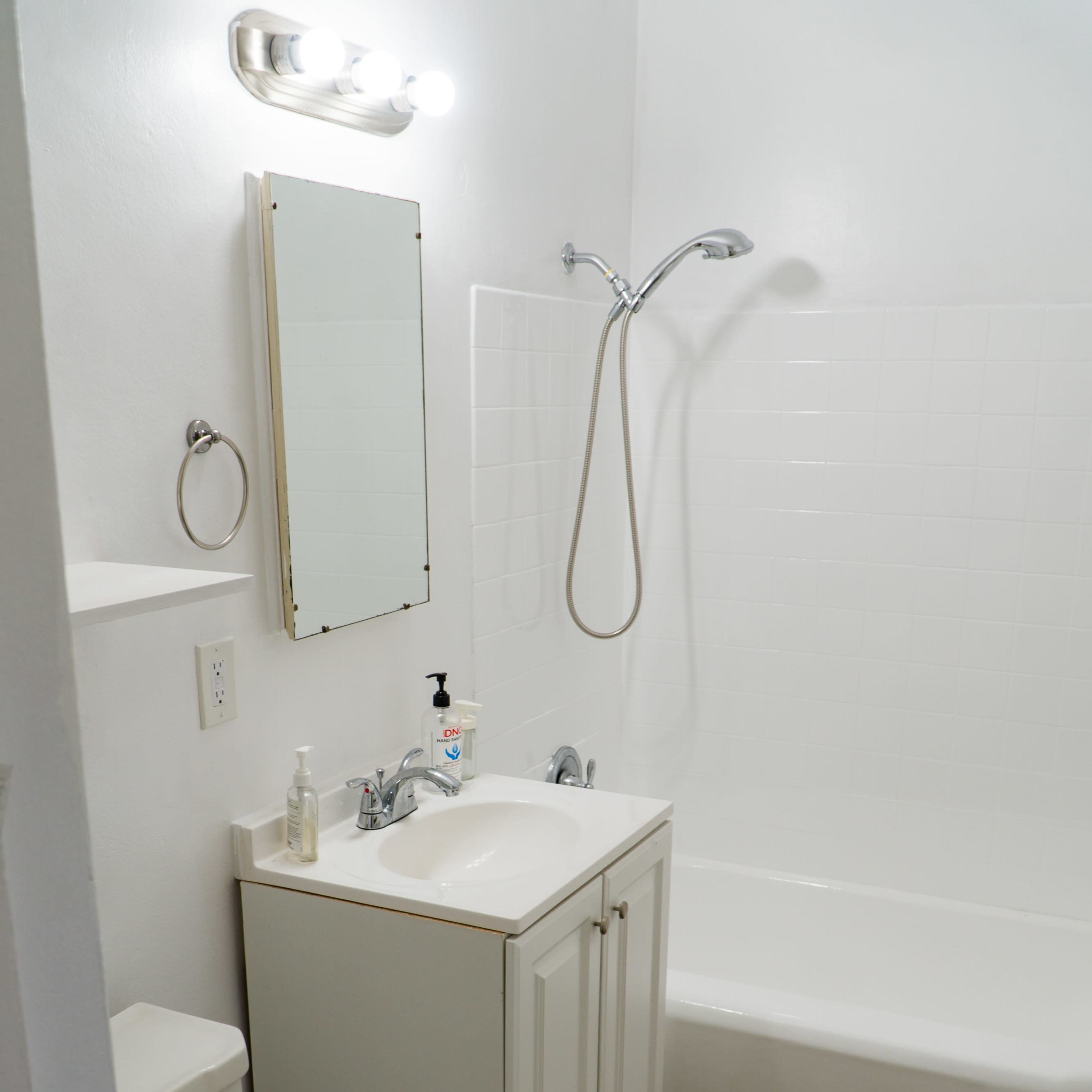 A small bathroom featuring a bathtub, a sink with a mirror above it, a toilet, and light-colored walls.