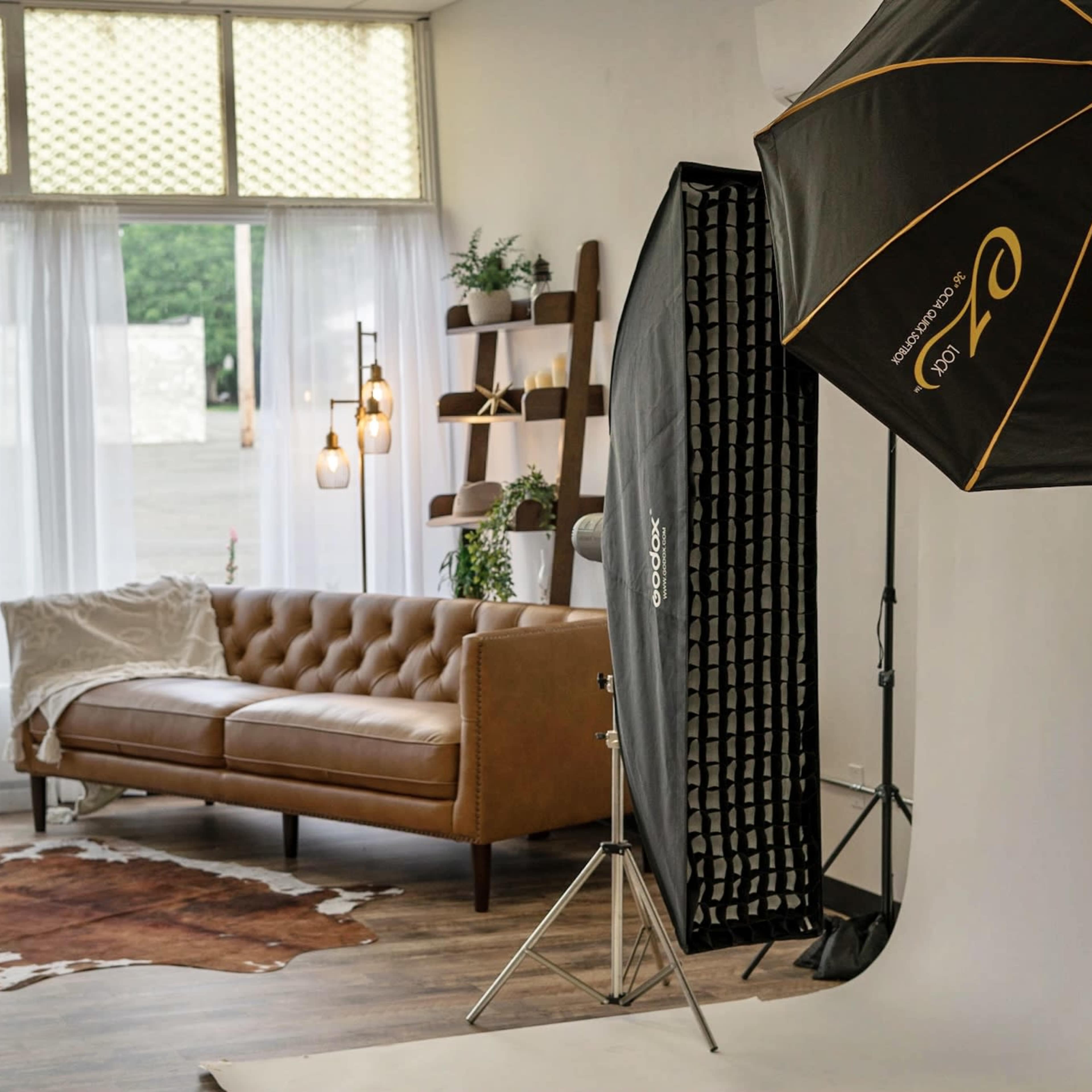 A photography studio setup with a brown leather couch, a backdrop, and lighting equipment in a softly lit room.
