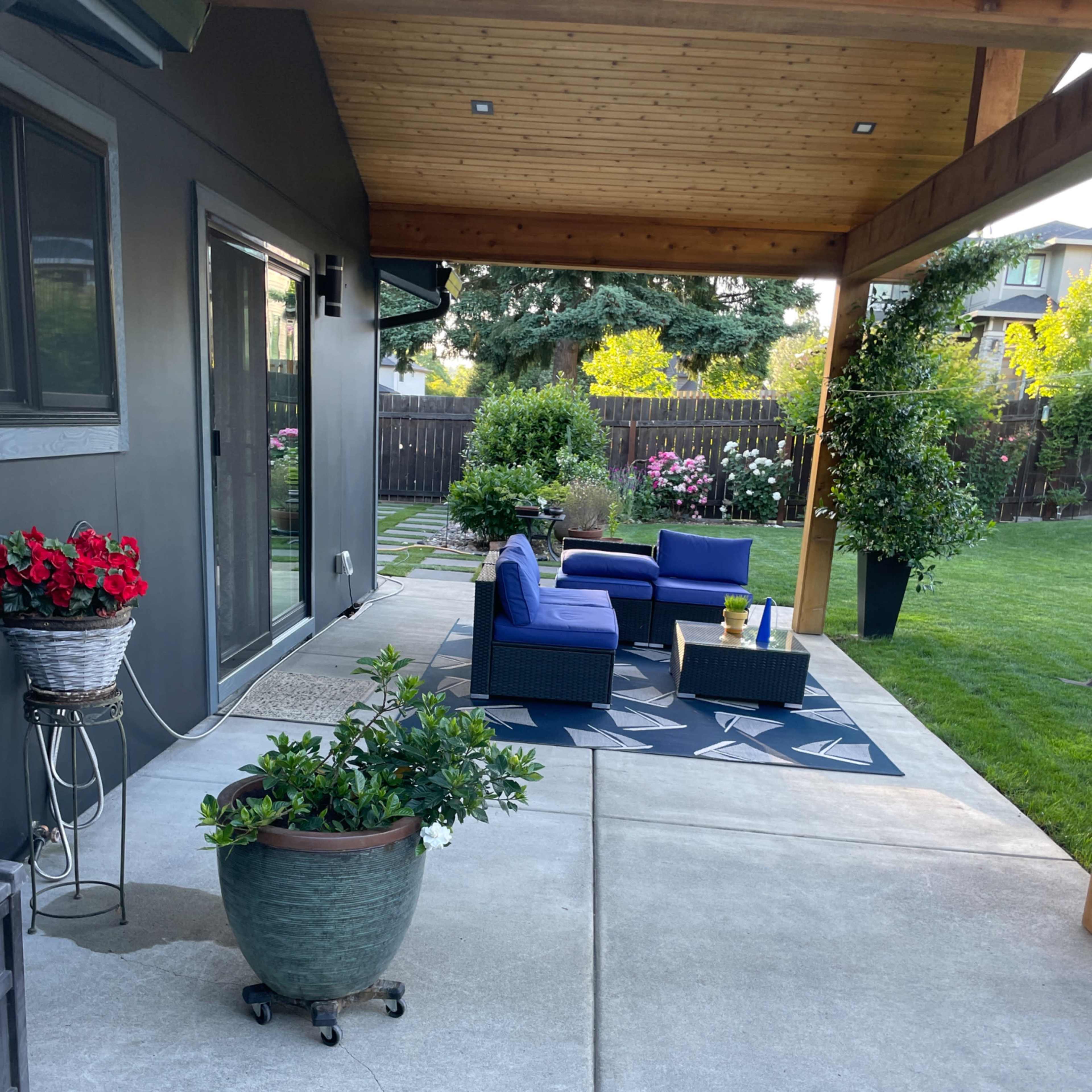 A patio area with two blue lounge chairs, a small table, and potted plants, surrounded by a well-maintained lawn and garden.