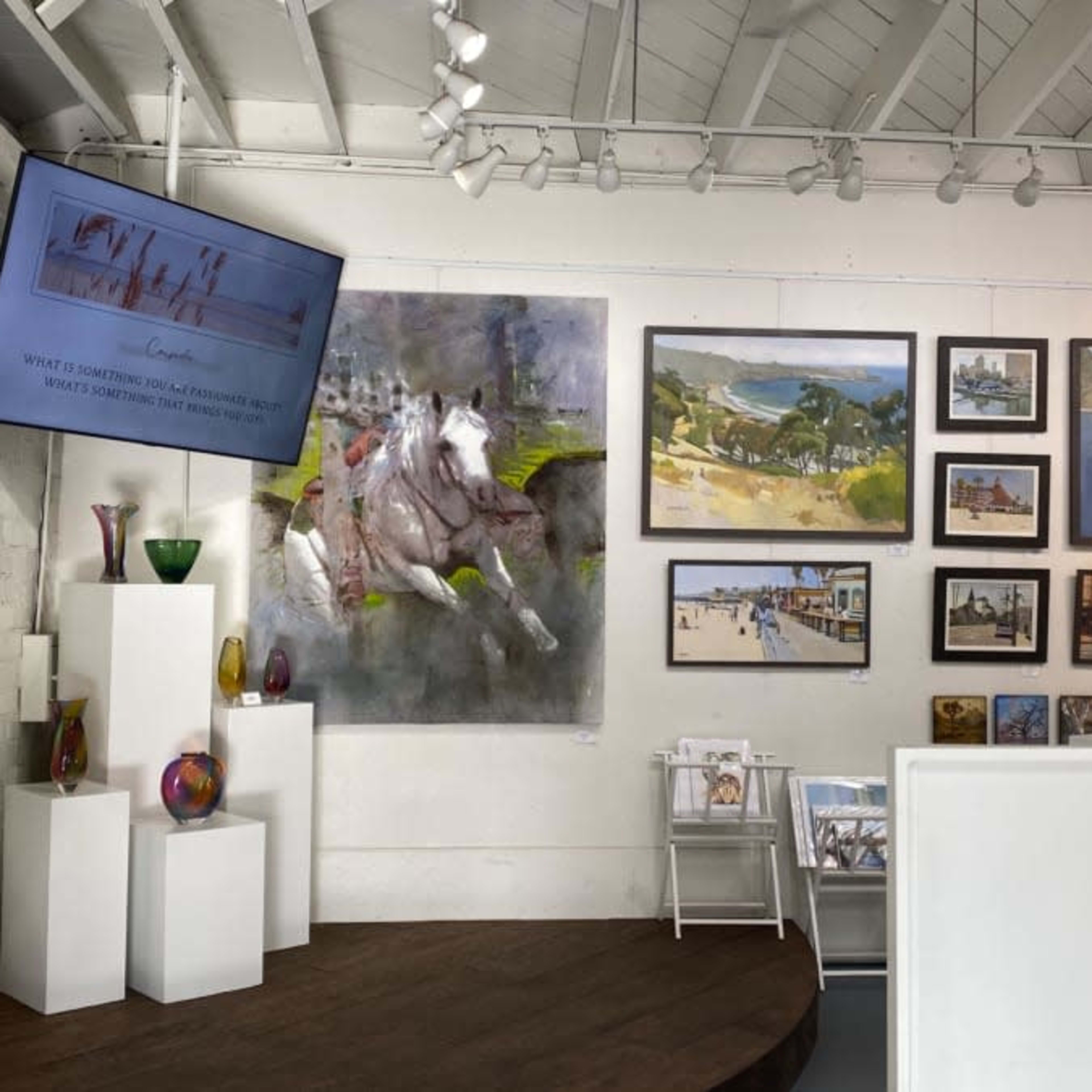 An art gallery interior with various paintings displayed on the walls and additional artworks arranged on shelves.
