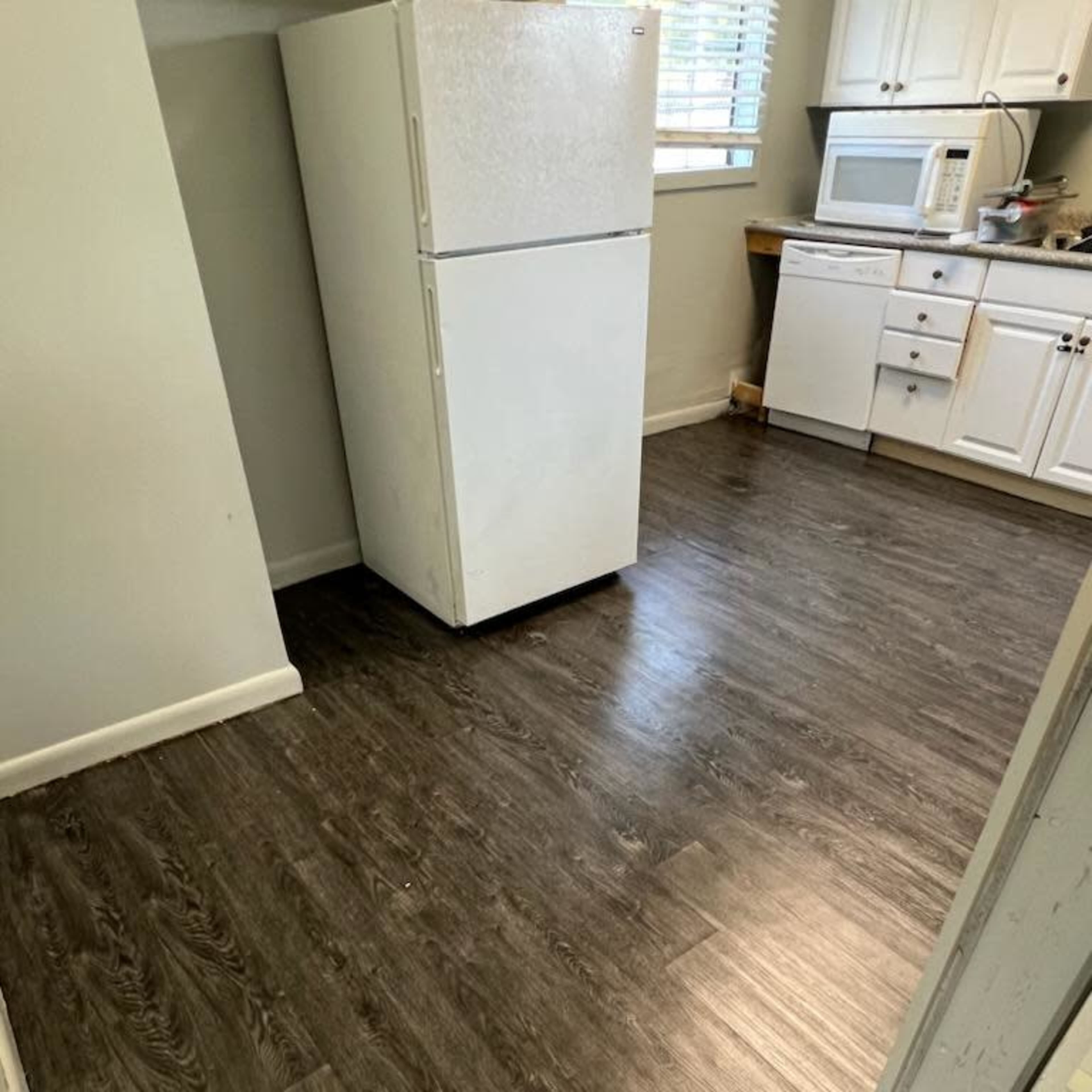 A kitchen with a white refrigerator and a microwave in a room featuring dark wood-like flooring.