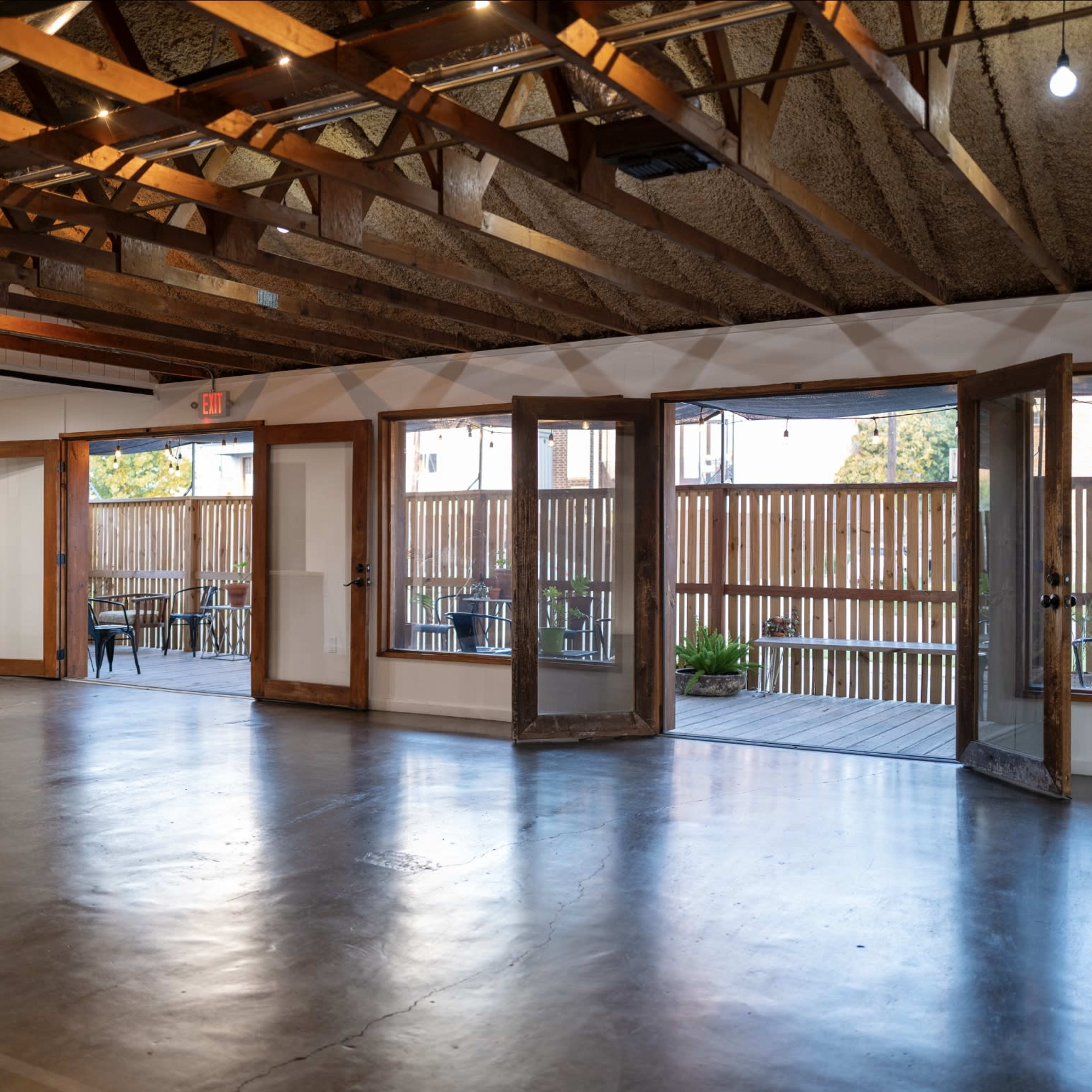 An open interior space with wooden beams, concrete flooring, and large double doors leading to an outdoor area.