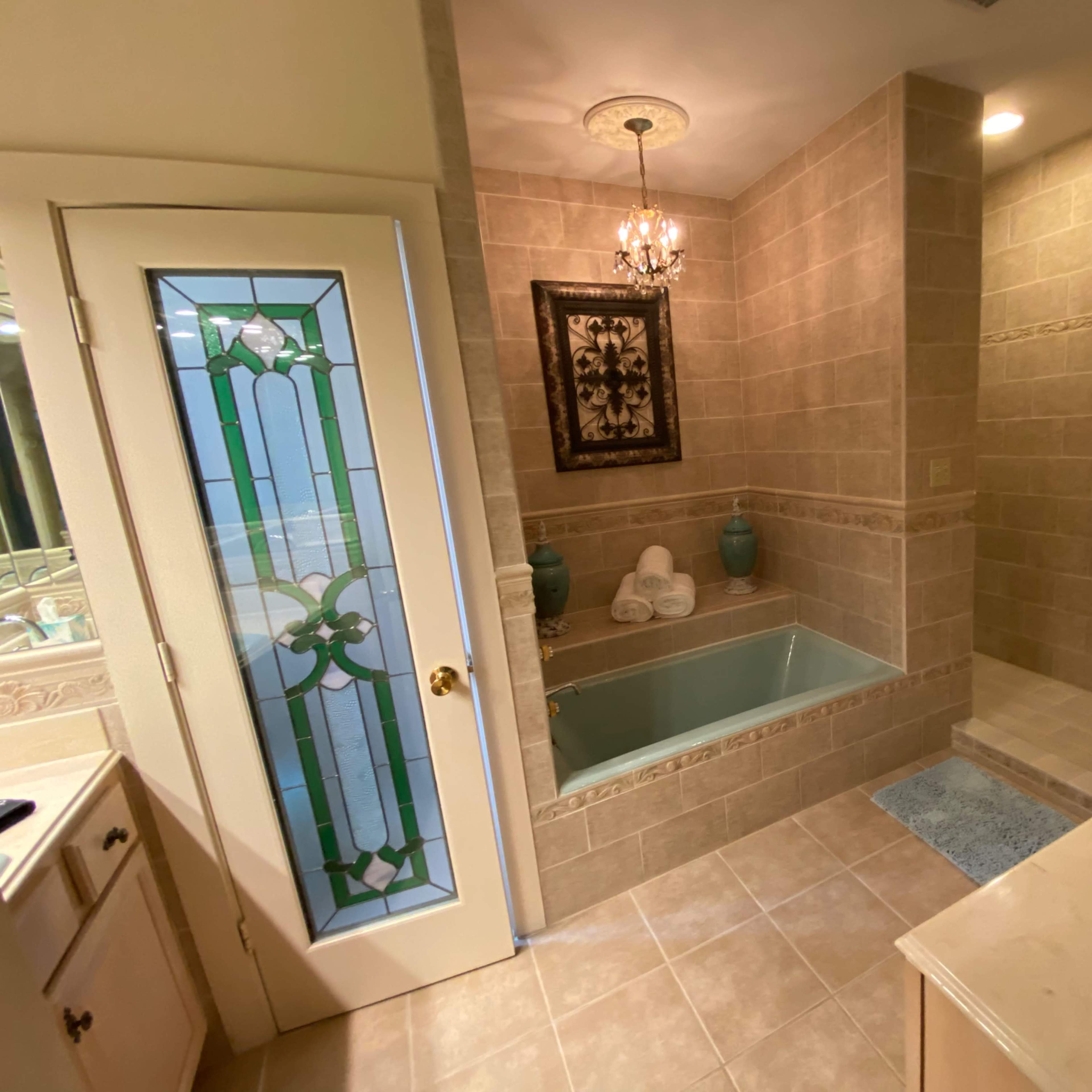 A bathroom featuring a bathtub with decorative tiles, a chandelier, and a decorative mirror.